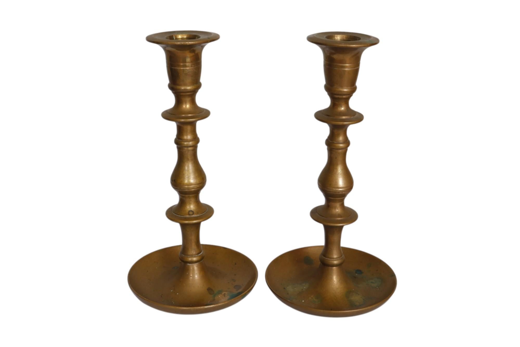 A pair of traditional turned brass candlestick holders. Sleek beveled capitals top baluster turned columns, decorated with two knops, above upturned drip-pan like bases. Light patina shows age.