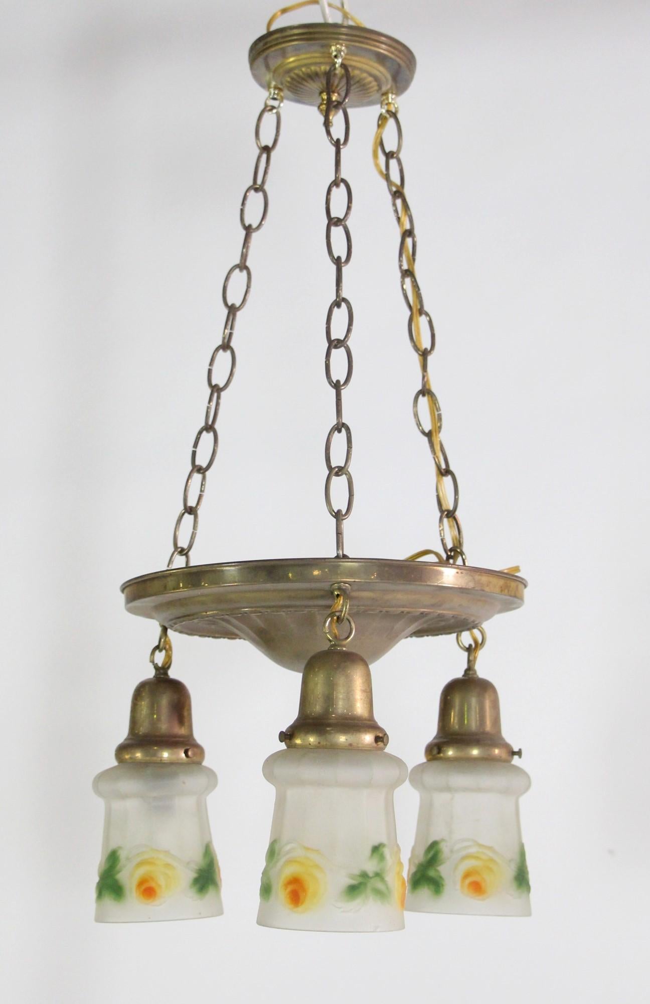Brass pendant light featuring 3 hanging lights with antique hand-painted glass shades. The shades are frosted with an orange, yellow and green floral detail. The hardware is newer making it wired and ready to go. This can be seen at our 400 Gilligan