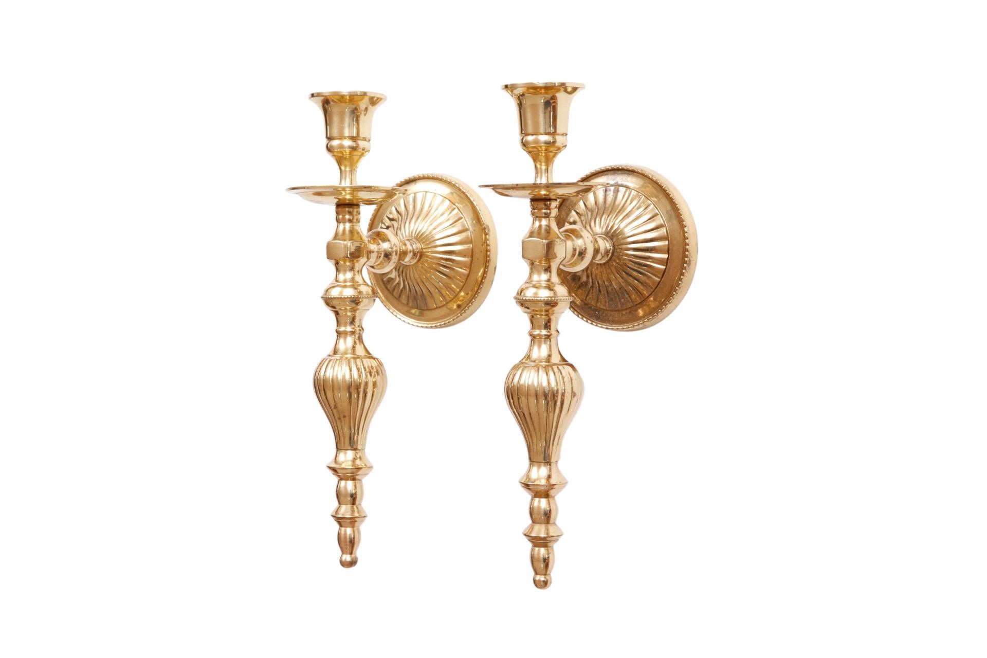 A pair of traditional brass candlestick sconces. Sleek capitals and drip pans are balanced with turned, reeded columns. Set on round reeded back plates. Dimensions per sconce.