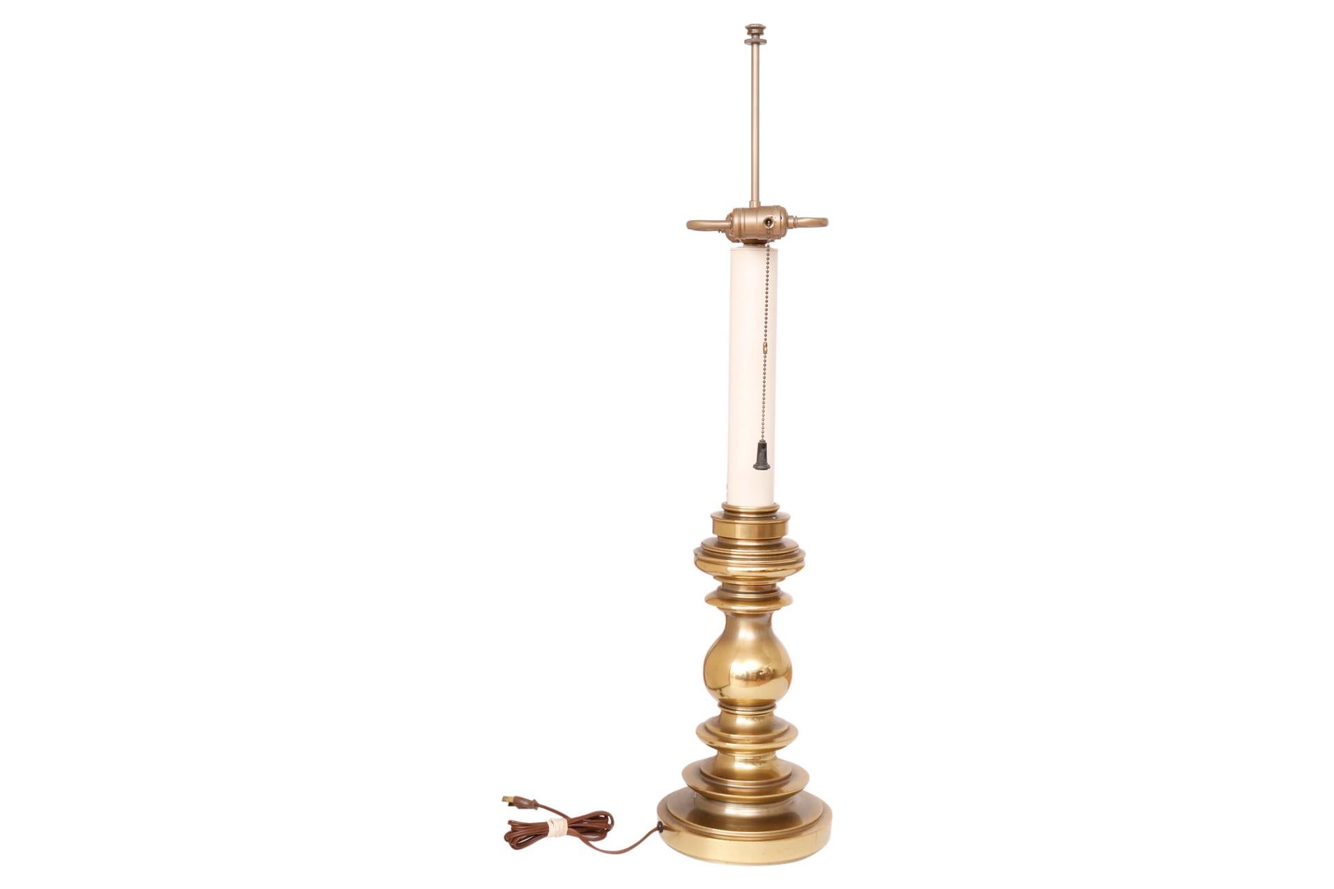 A traditional brass table lamp made by Stiffel. The central column is highly turned brass with a thick round beveled base. Above is a sleek cream column topped with opposing sockets. To support the shade is a slender brass post with a small cap