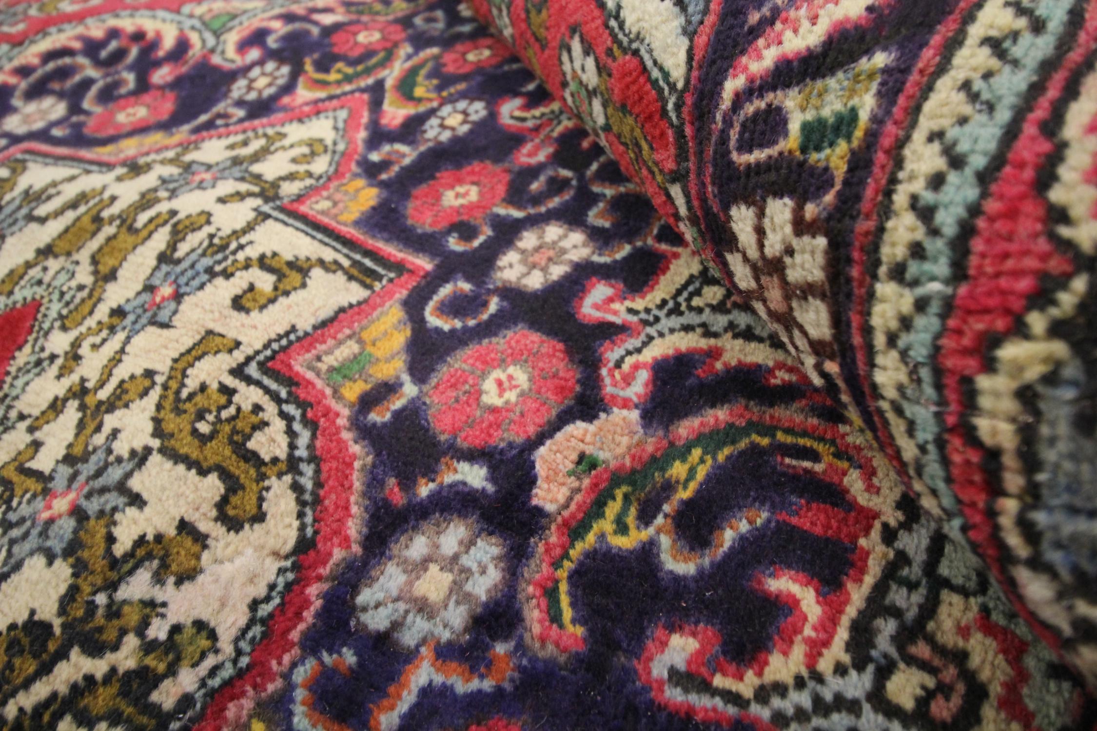This rich red rug is a traditional red wool carpet woven by hand in the late 20th century, Circa 1970. The design has been woven on a rich red background with accents of brown, cream, blue and green that make up the radiant decorative medallion and