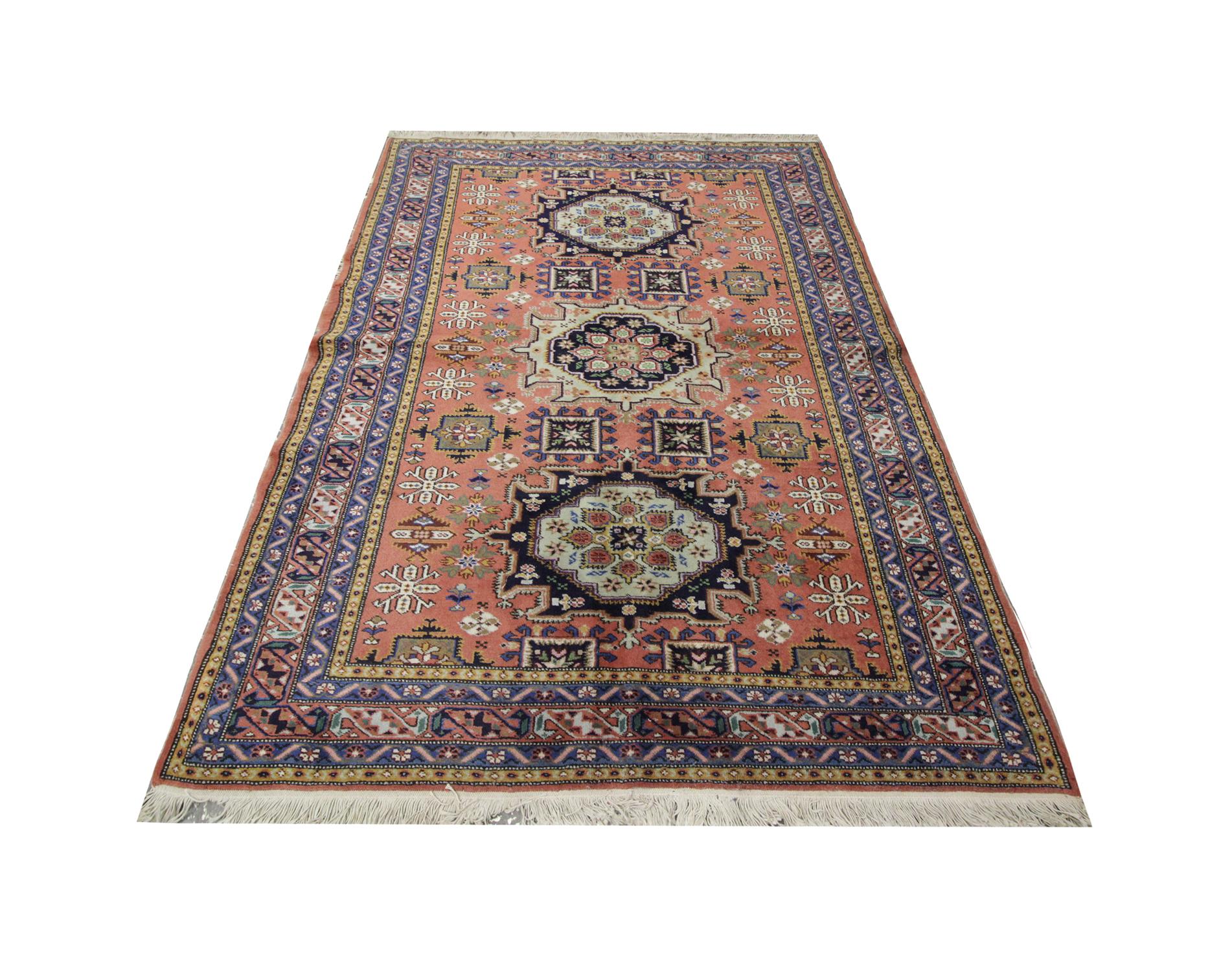 This Oriental rug vintage area rug features a highly detailed, colorful, central design which majestically floats on a background of subtle orange. Encompassed by a strong multi-layered bold print border woven in deep blues, white and yellow. This