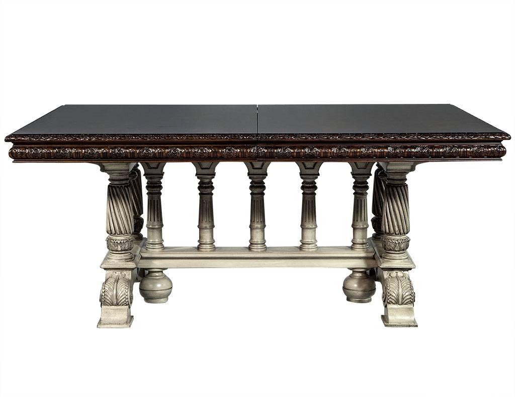 This Tudor style dining table is composed of mahogany solids and veneers with a flamed top and hand carved flowered edge. The pedestals are also hand carved and finished in a cream color. In excellent restored condition this table is perfect for a