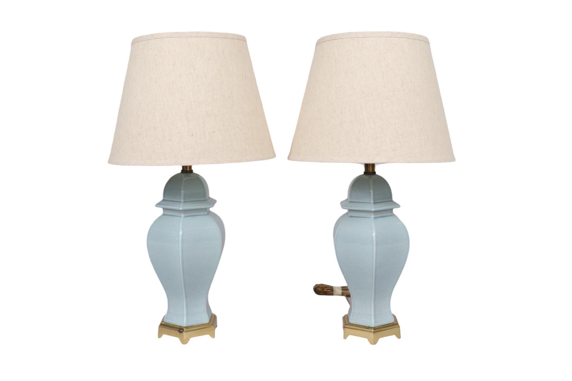 A pair of traditional ceramic table lamps. Cast with a hexagonal body and a beveled cap finished in a baby blue craquelure glaze, set on a simple brass base. Empire cylinder shades are in an ecru linen. Each lamp measures 7