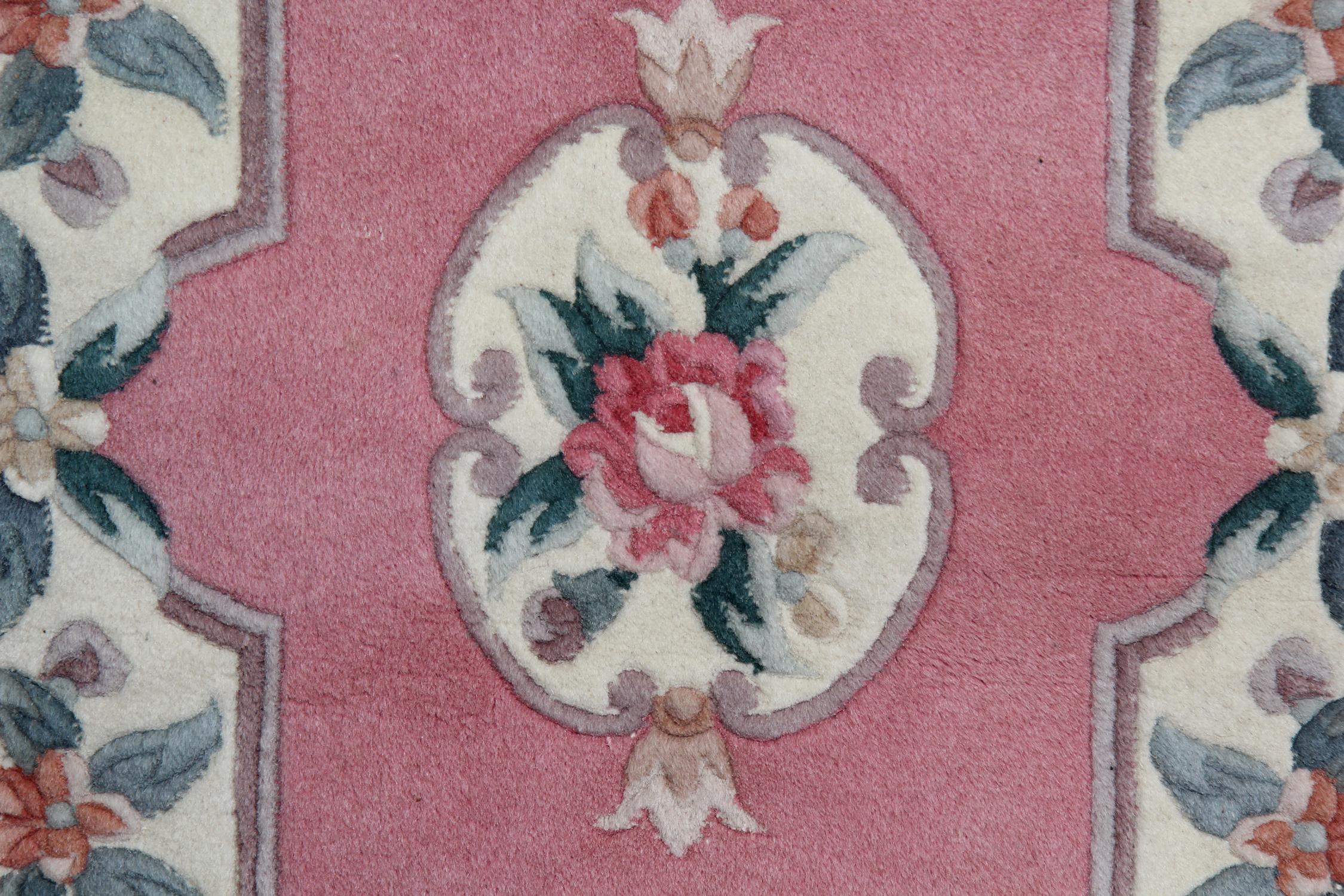 Cet élégant tapis fait main a été fabriqué dans les années 1990 en Chine. Le motif central a été tissé sur un champ rose avec des accents de pêche, de violet et de vert qui composent le médaillon floral et le motif symétrique qui l'entoure. Une