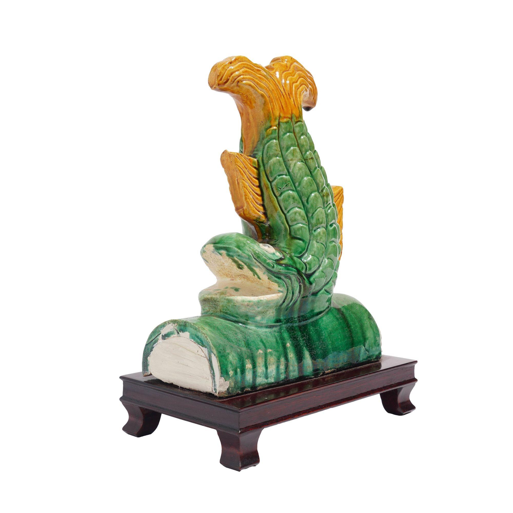 Traditional Chinese ceramic fish form roof tile terminal, glazed in green and marigold yellow & mounted on a mahogany footed stand.
China, 20th century.

Dimensions: 8-1/4” L x 5-1/4” W x 12” H