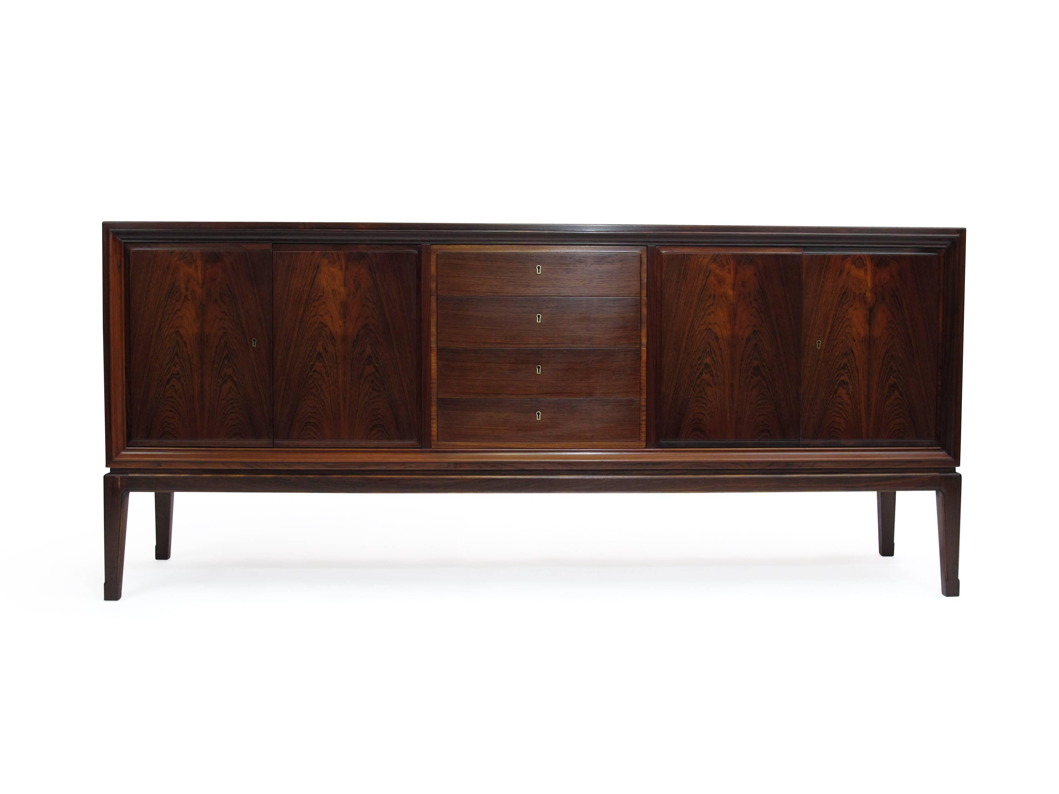 Finely crafted credenza of dark rosewood with pattern match across front of doors. Fully locking doors and centre drawers. The double doors open to reveal a birch interior with an adjustable shelf. Raised on tapered legs.
