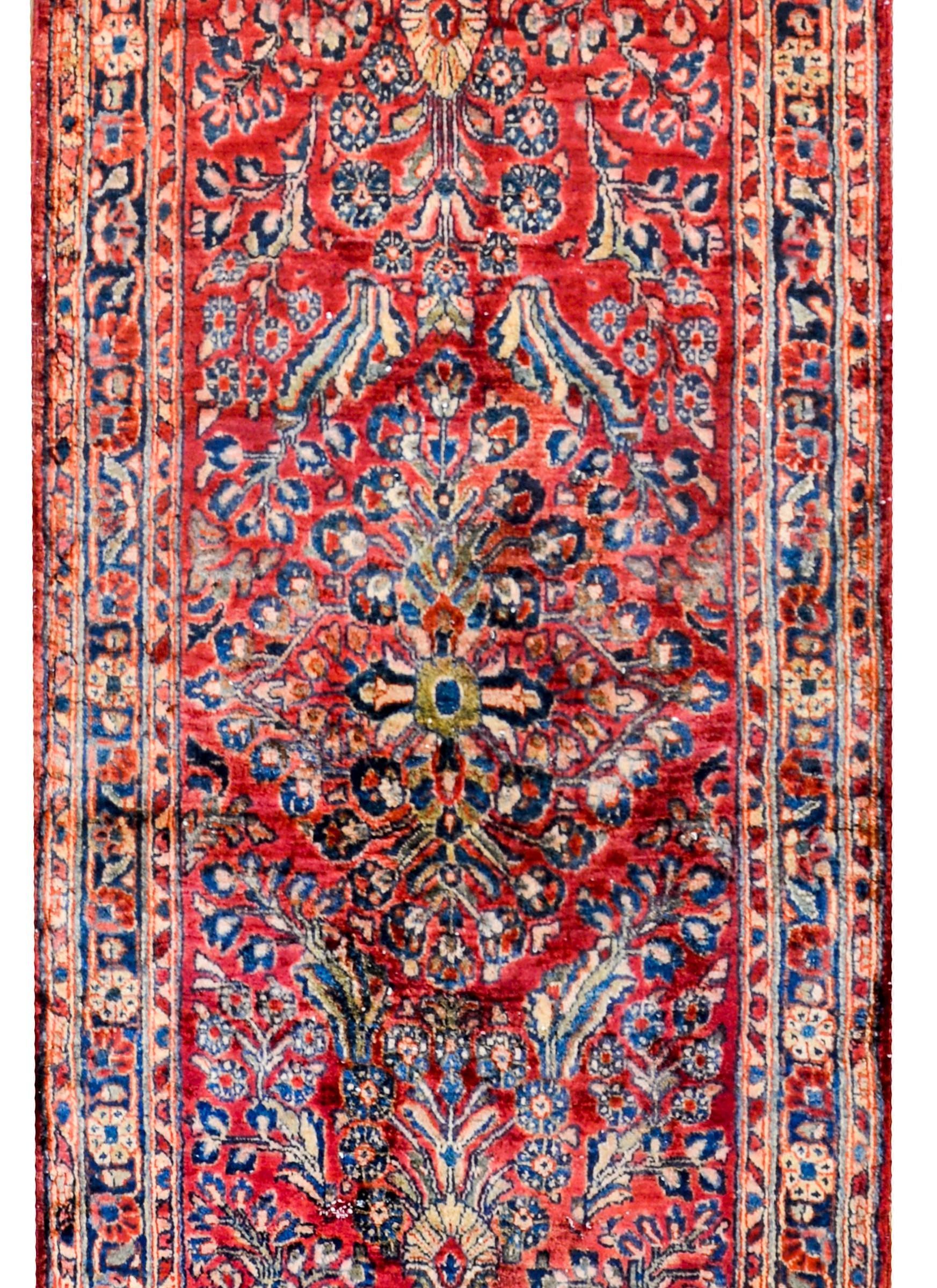 A traditional early 20th century Persian Sarouk runner with a mirrored floral pattern with myriad flowers and vines woven in cranberry, gold, indigo, taupe and green vegetable dyed wool. The border is sweet, with myriad flowers and leaves flanked by