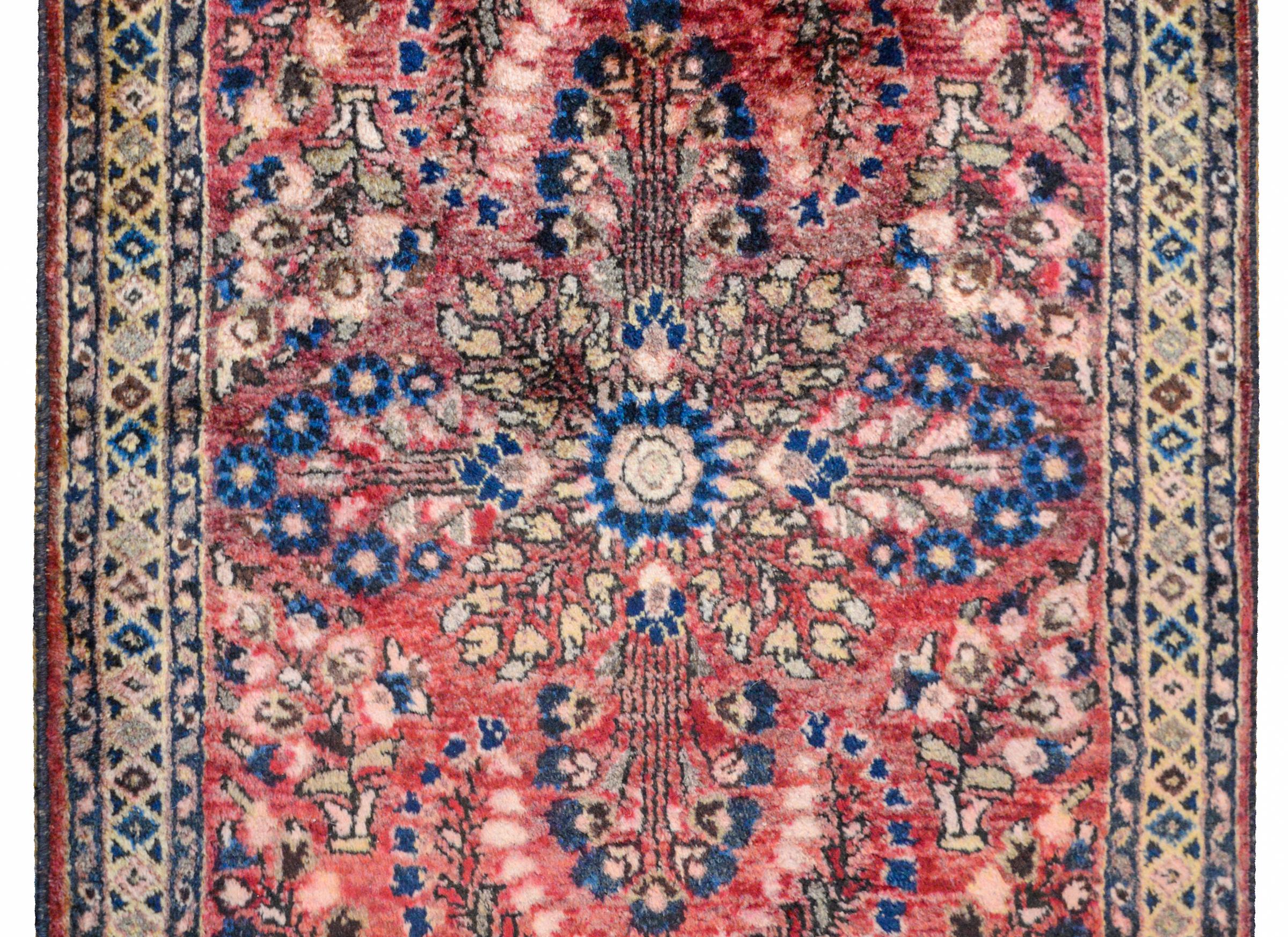 A traditional early 20th century Persian Sarouk rug with a mirrored tree-of-life pattern woven in indigo, brown, beige, and pink vegetable dyed wool on an abrash cranberry background surrounded by a simple geometric border flanked by a pair of