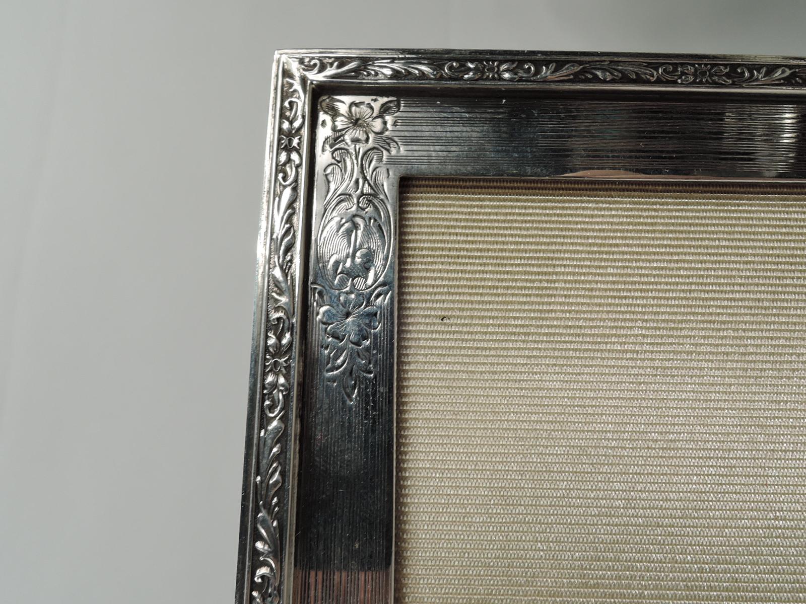 Edwardian Classical sterling silver picture frame. Made by Birks in Canada in 1954. Rectangular window in flat surround with engine-turned wraparound lines and engraved flowers and scrolls; Raised rim with low-relief flowers and scrolls. Central
