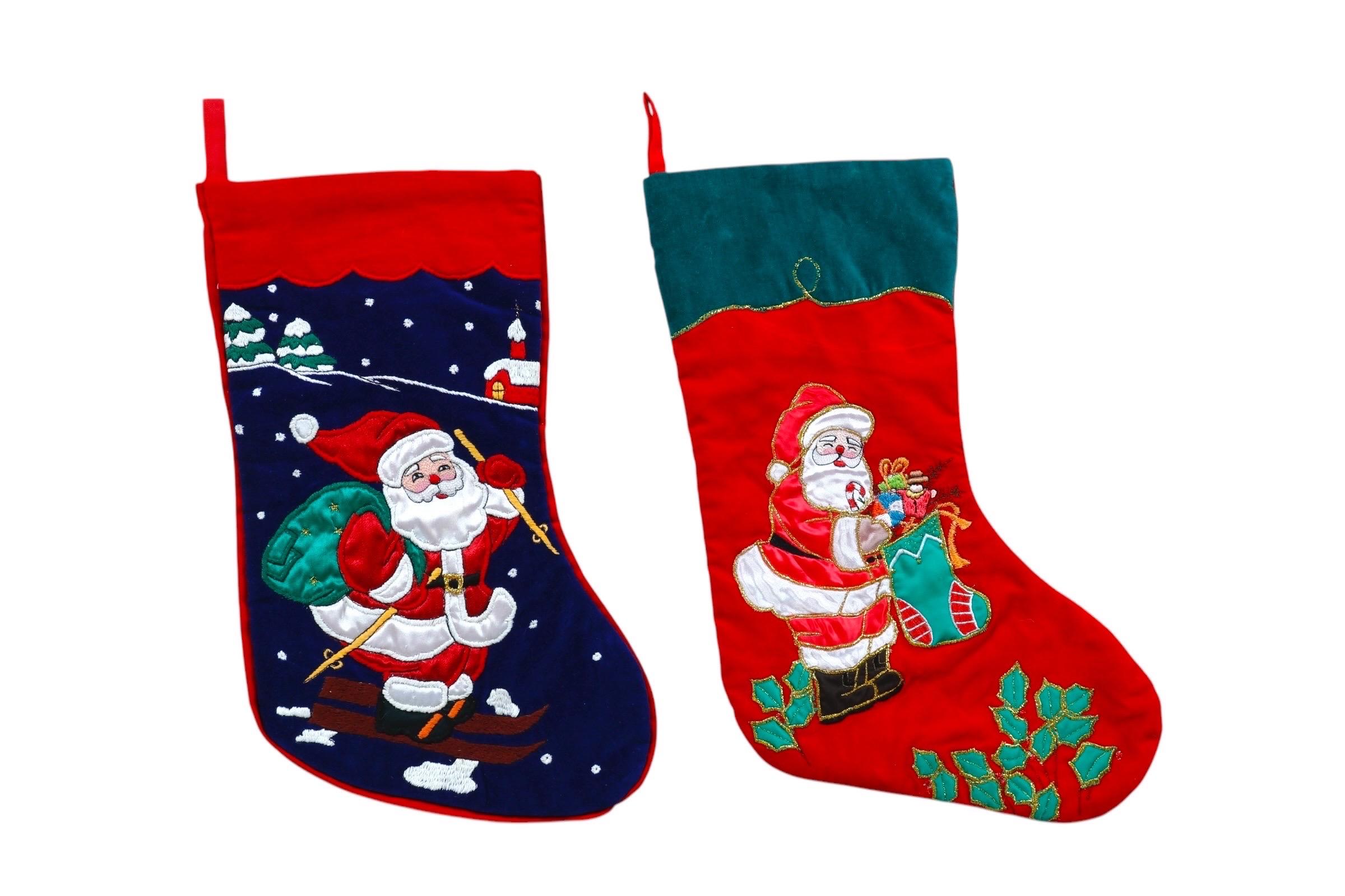 Ein Set aus zwei traditionellen gesteppten und bestickten Weihnachtsstrümpfen. Jeder Strumpf zeigt den rot gekleideten Weihnachtsmann. Auf dem einen ist er mit einem grünen Sack auf Skiern unterwegs, mit schneebedeckten Bäumen und einem Haus vor