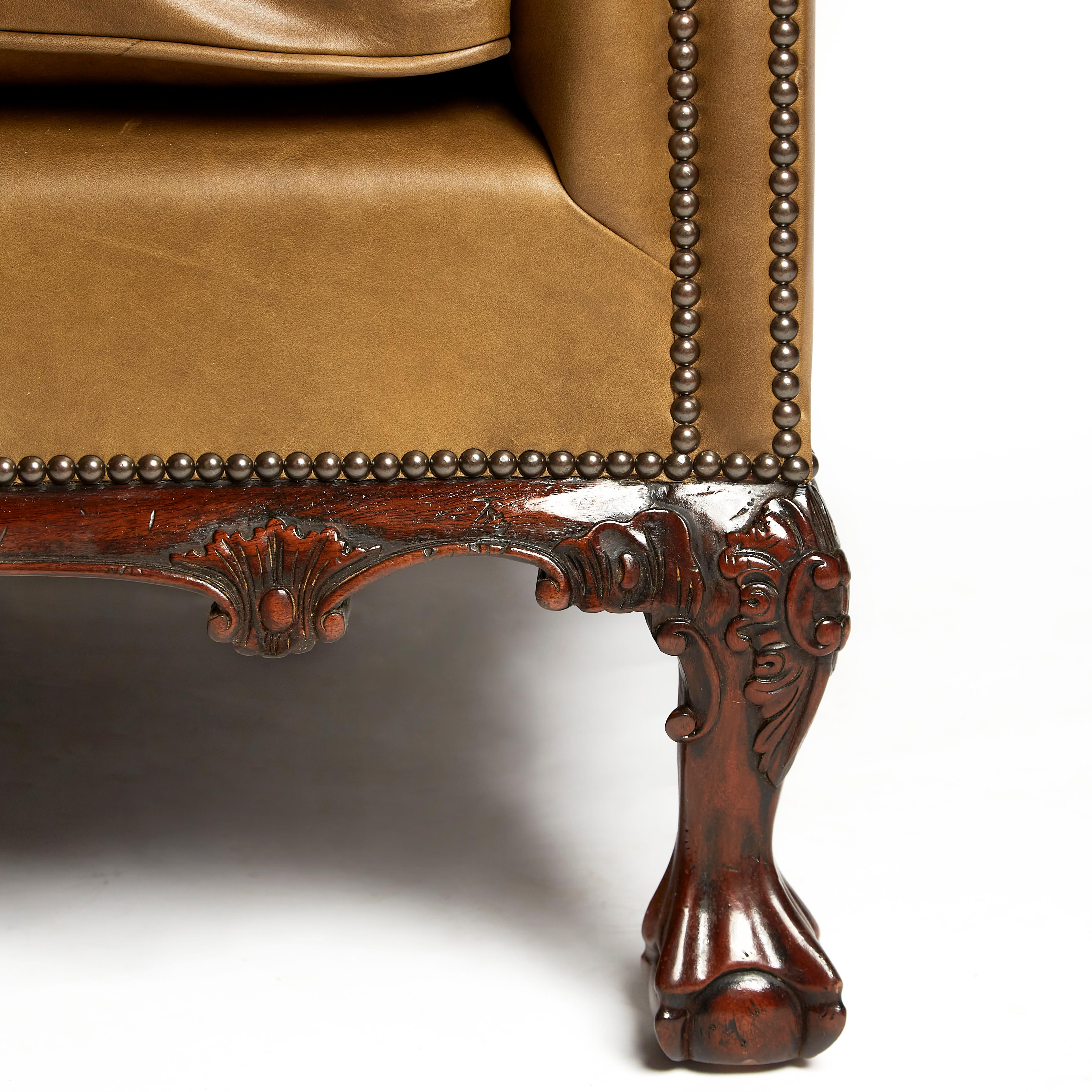 Ce magnifique canapé chesterfield anglais de style traditionnel présente un dossier façonné et boutonné et deux coussins d'assise séparés en cuir lisse. Le canapé est doté d'une magnifique plinthe centrale sculptée et repose sur des pieds à boule et