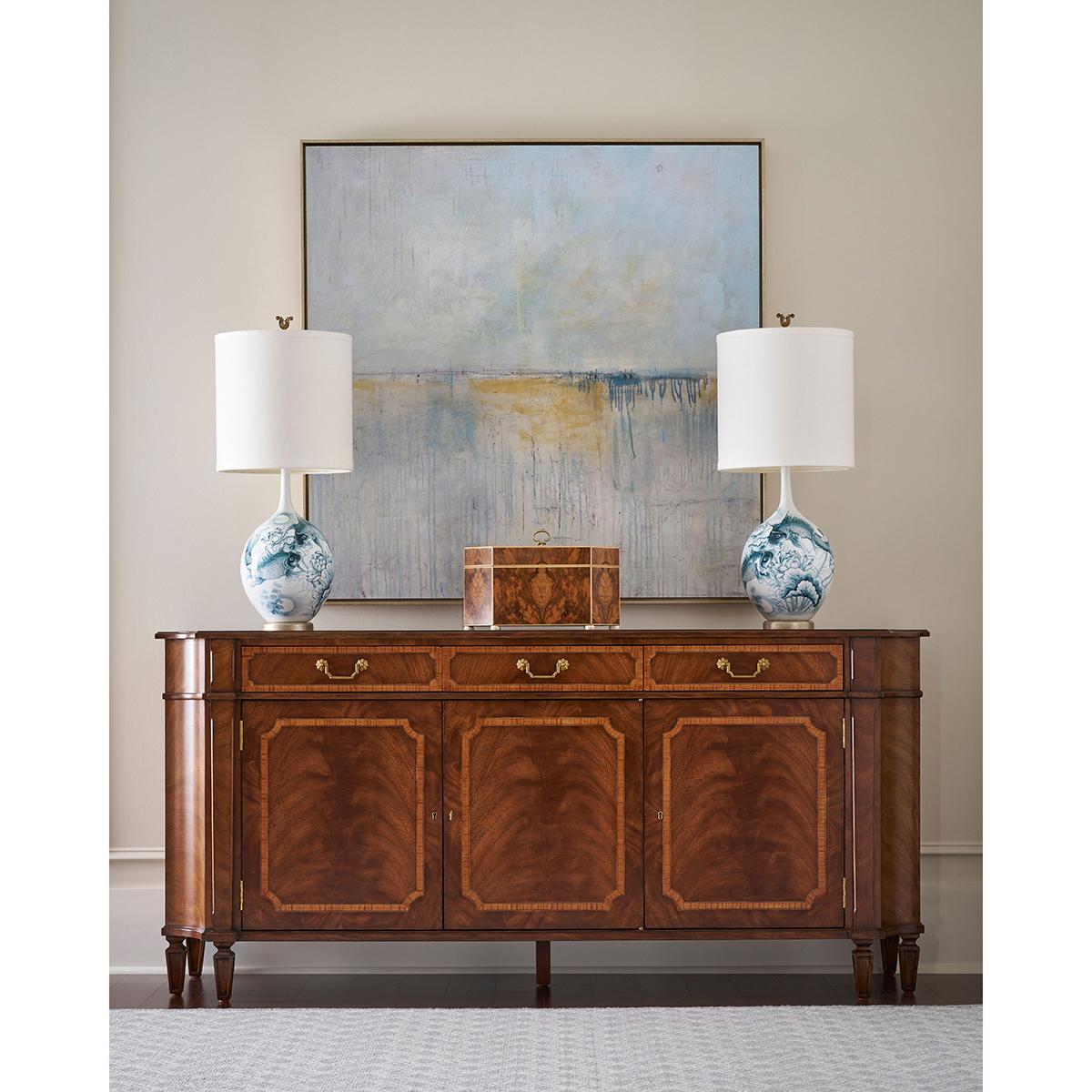 Magnificent figured wood draws the eye across its three-door buffet form, enhanced by a medium brown finish that brings depth and richness to the veneered surfaces. The breakfront silhouette and finely inlaid paneling emphasize its neoclassical