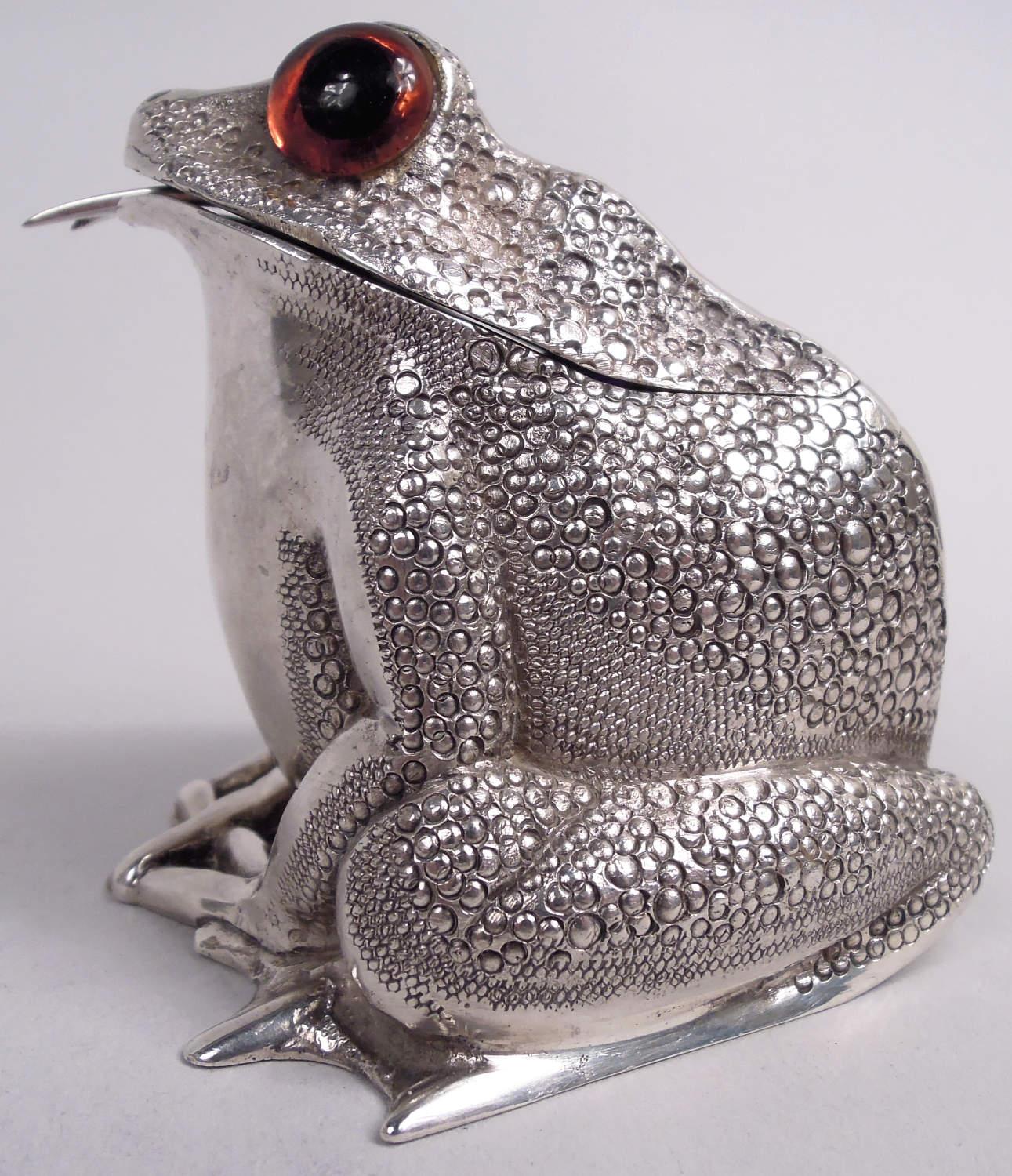 English sterling silver figural mustard pot, 1966-67. A squatting, smirking frog with glass exophthalmic eyes and scaly back and tucked-under hindlegs; breast and forelegs plain. Hinged head; cobalt glass liner. Gaping mouth inserted with spoon