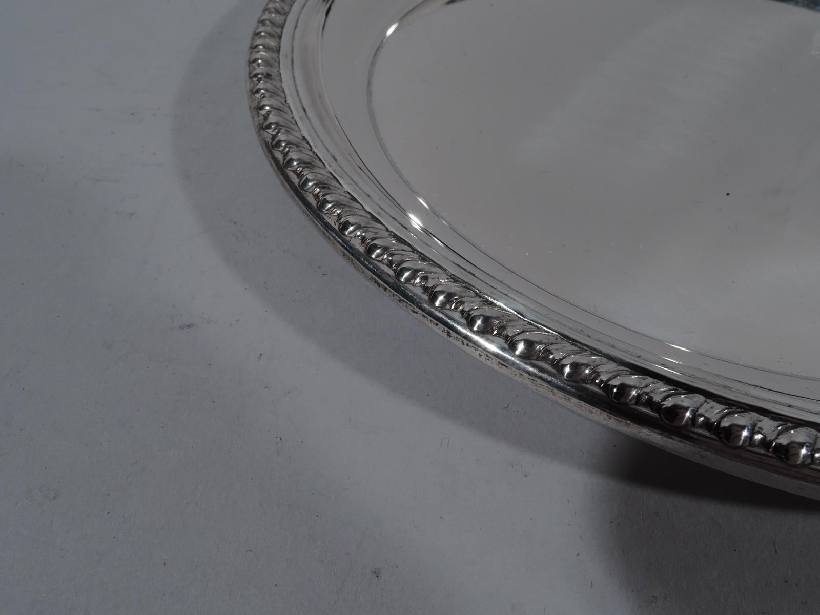 Georgian-style sterling silver tray. Retailed by Cartier in New York, circa 1950. Round with chased gadrooned rim. Traditional with nice heft. Marked “Cartier” and “Sterling”. Heavy weight: 9.5 troy ounces.