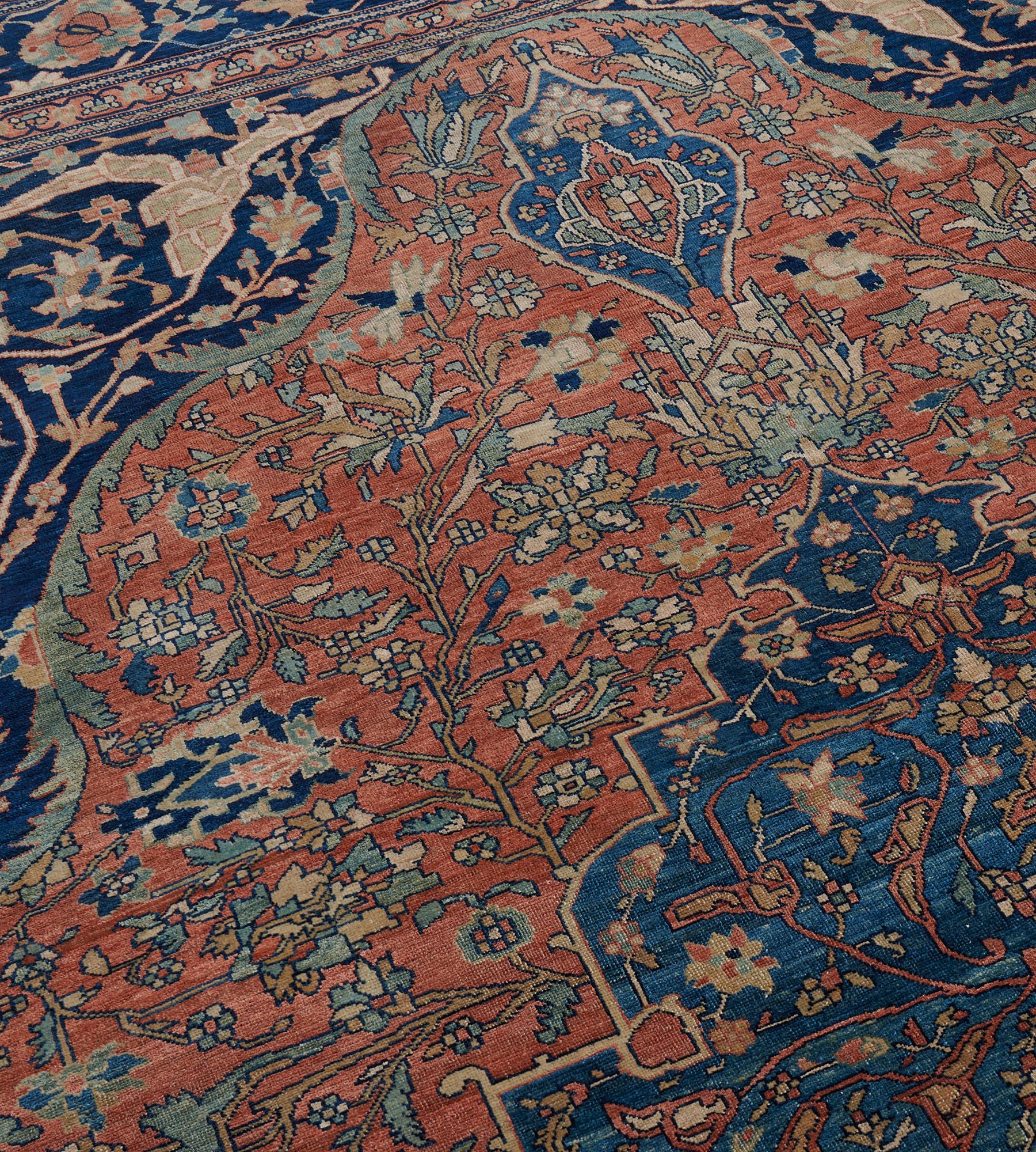 This antique Persian Sarouk rug has a brick-red field with a delicate palmette and leafy vine around a large central light blue cusped medallion and palmette pendants, a central brick-red lozenge medallion with a delicate scrolling palmette vine