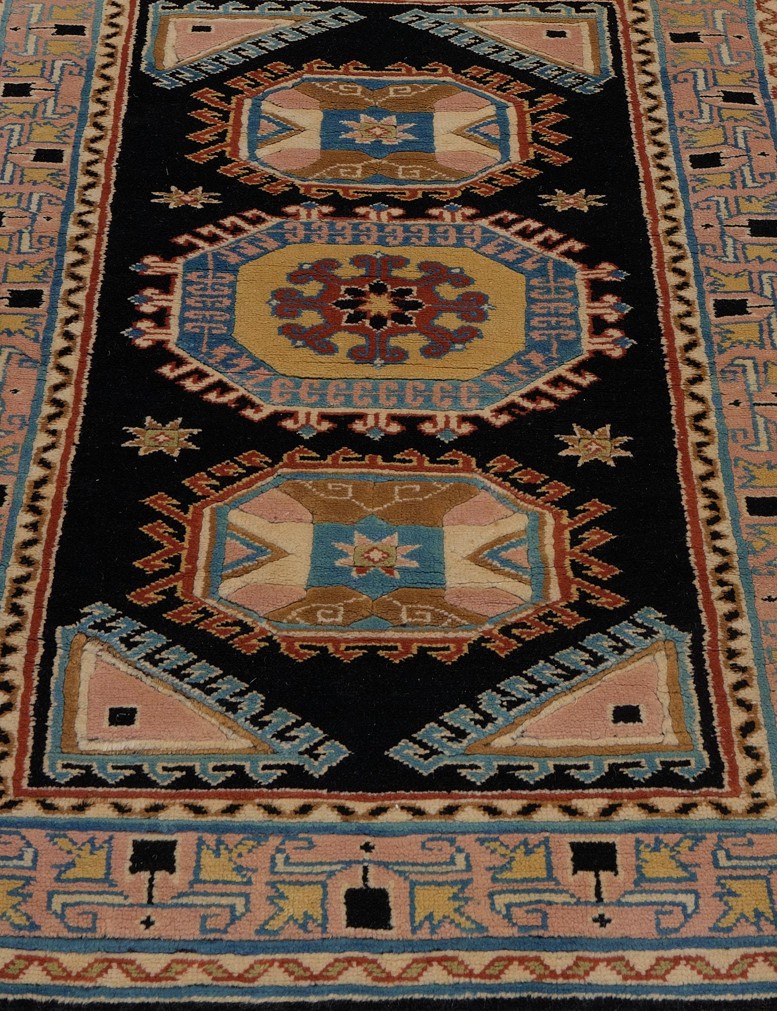 This traditional hand-woven Turkish rug has a shaded charcoal field enclosing a central column of three serrated hexagonal medallions, in a shaded pale-pink geometric vine border, between tonal zig-zag stripes.
