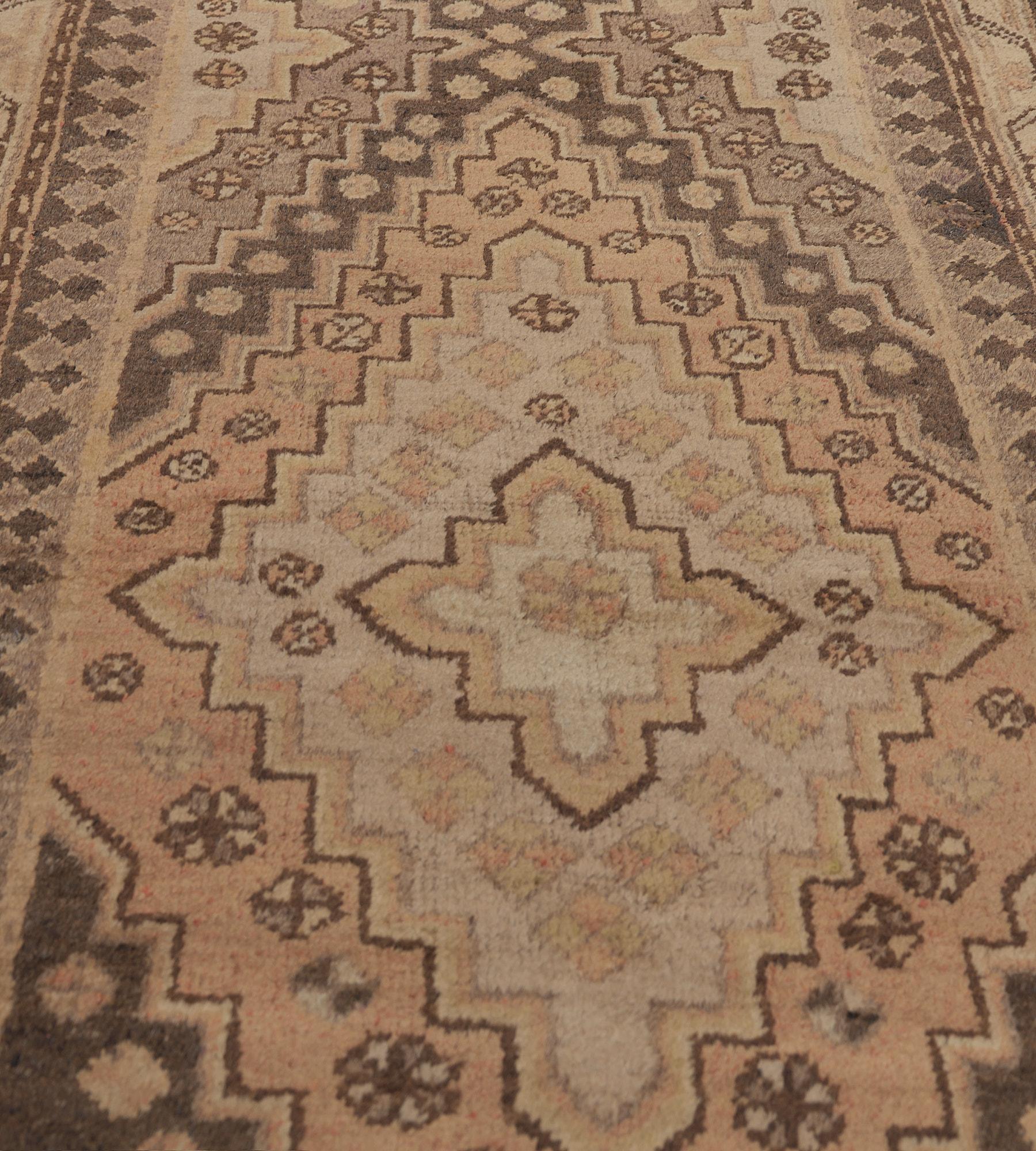 This antique, circa 1900, Khotan runner has a field with a pair of linked stepped lozenges with central buff-brown lozenges surrounded by an ivory and terracotta lozenges with flowerheads and an outer shaded chocolate-brown lozenge with small floral