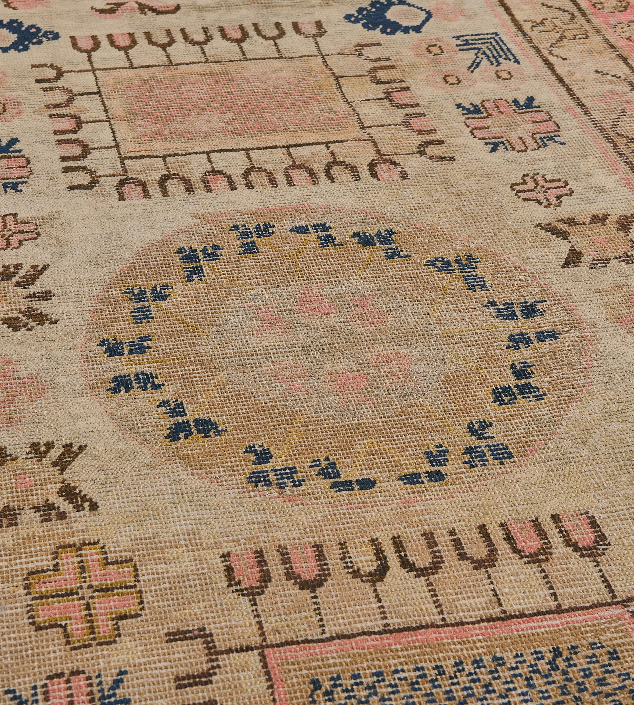 This traditional hand-woven Samarkand Khotan rug has a wheat field of geometric polychromatic floral sprays and pomegranate vines with roundel medallion enclosing polychrome rosette, in a shaded dusty beige floral vine border, enclosed by a shaded