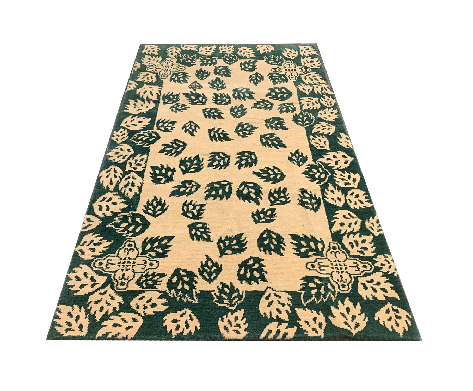 This wool pile carpet is an antique piece woven by hand in India in the early 20th century. The design features a simple colour palette of green and cream and has been composed with a symmetrical leaf pattern through the centre and a repeating leaf