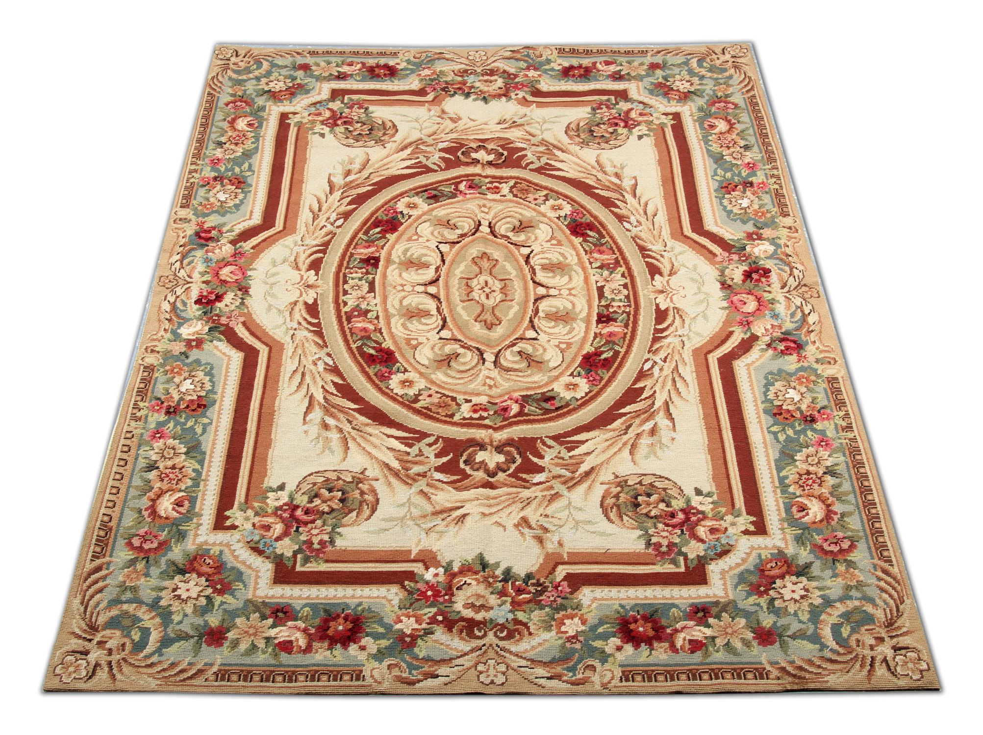 This highly-decorative Aubusson rug features a beautifully woven floral design in green, deep red, beige, and brown colors. The border that encloses the central design features a green background and a decorative floral repeat pattern. Both the