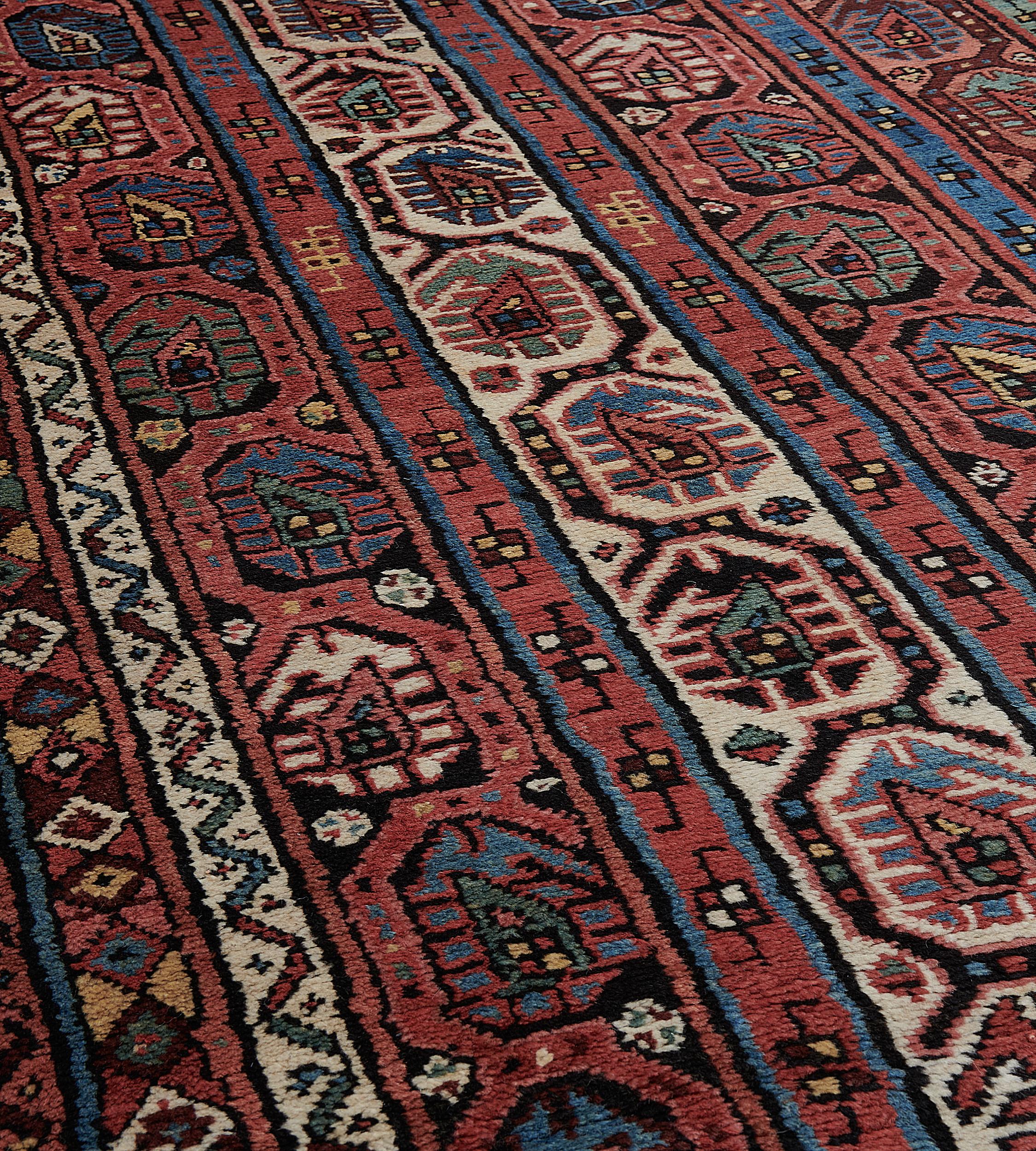 This traditional hand-woven Caucasian Kurd- Kurah rug has a shaded brick red and ivory field of four geometric stylized paisley columns, separated by inner geometric paisley stripes, in a polychromatic triple geometric stripe border.