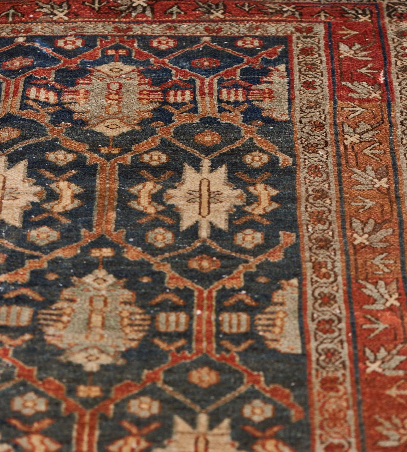 Ce tapis persan traditionnel Malayer, tissé à la main, présente un champ marine foncé avec un motif général de treillis à losanges en escalier entourant des médaillons liés, dans une bande rouille avec une bordure florale polychrome entre des bandes