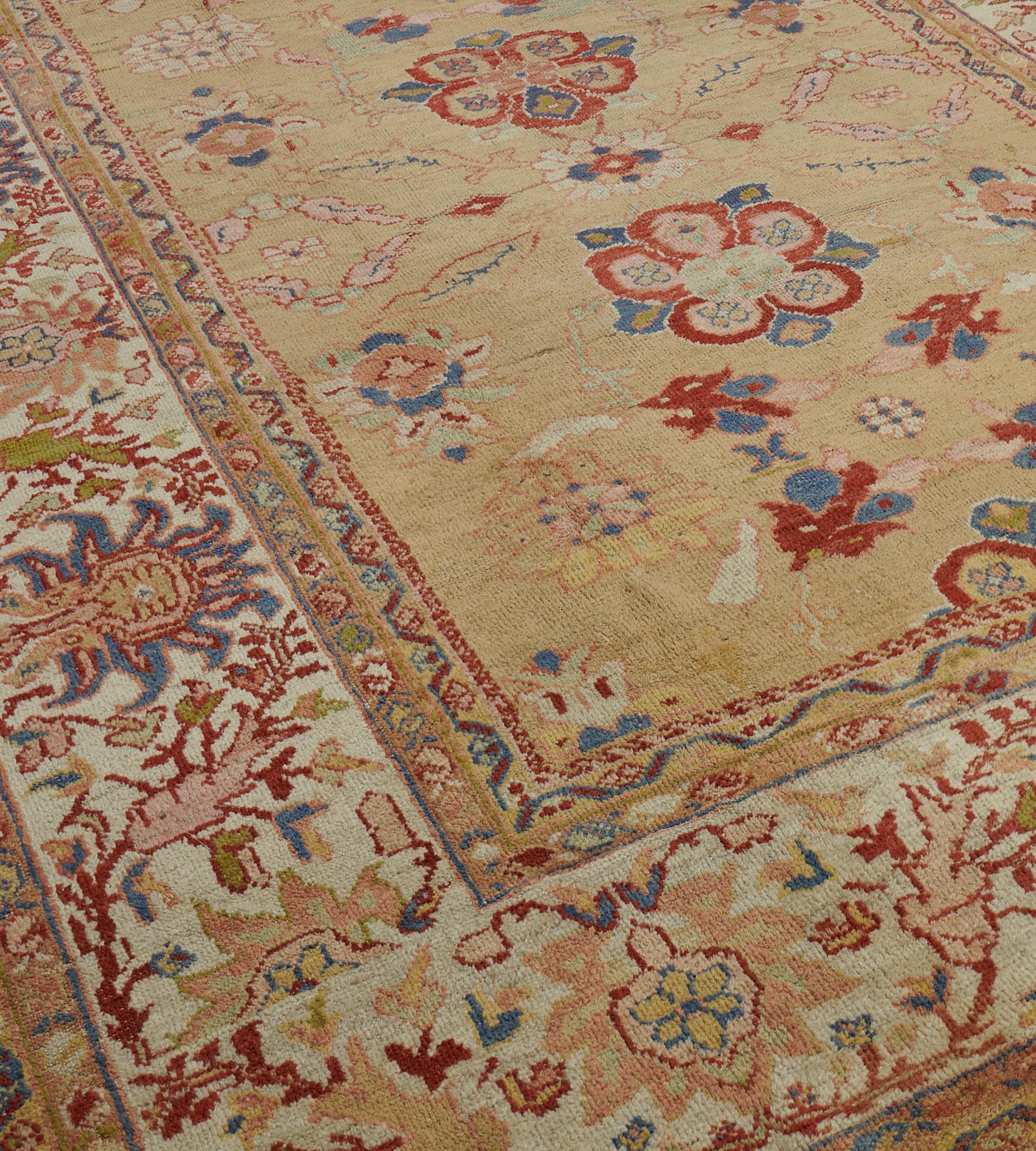This traditional hand-woven Persian Ziegler Sultanabad rug has a sandy-yellow field with a central column of brick-red open flowerheads and floral motifs flanked by similar smaller ivory flowerheads, in a broad ivory border of polychrome palmette