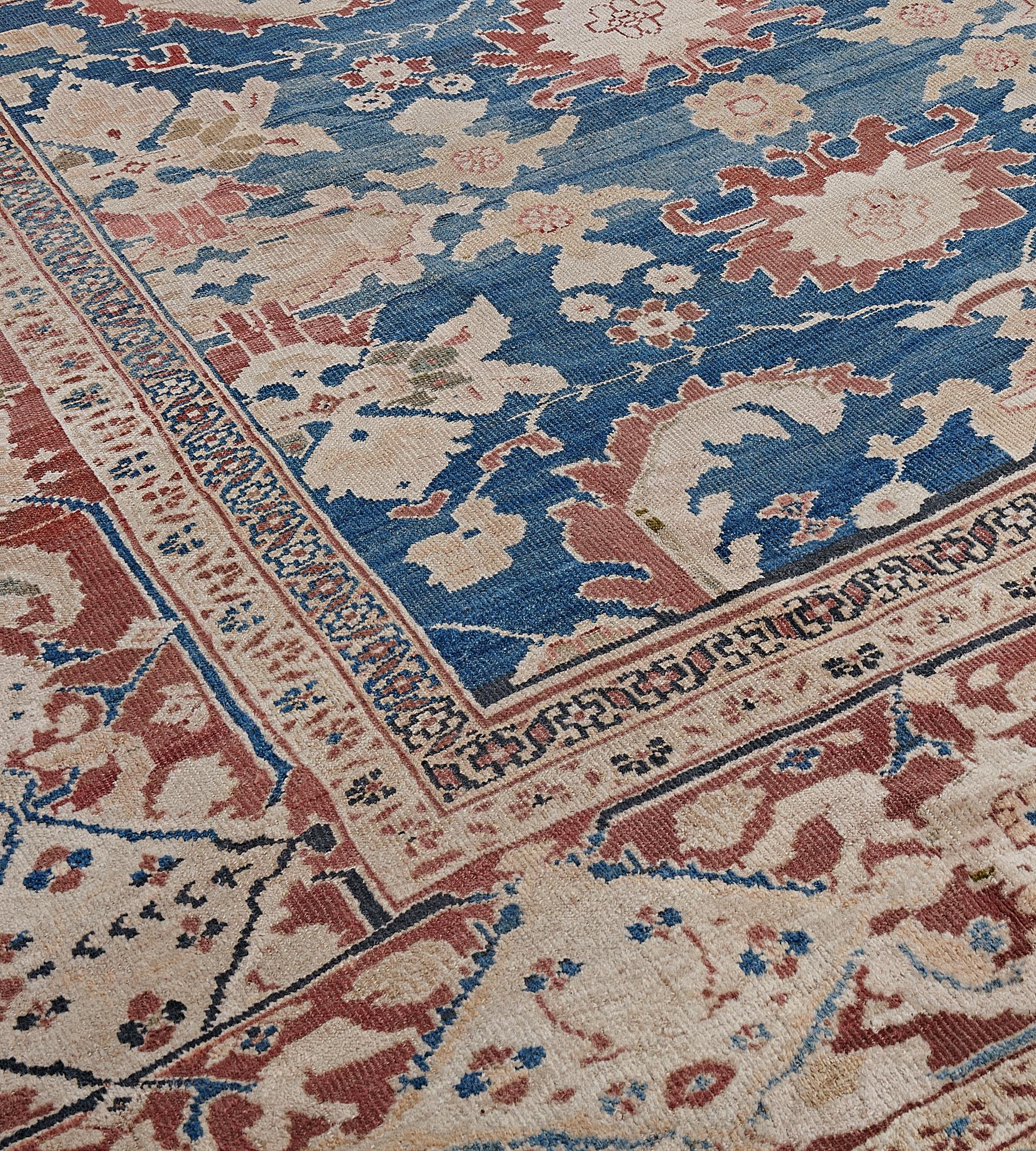 This traditional hand-woven Persian Ziegler Sultanabad rug has a shaded medium blue field with symmetrical rust and cream floral motifs and serrated curling leaves with subtle accents of artichoke-green foliage, in a broad rust border with
