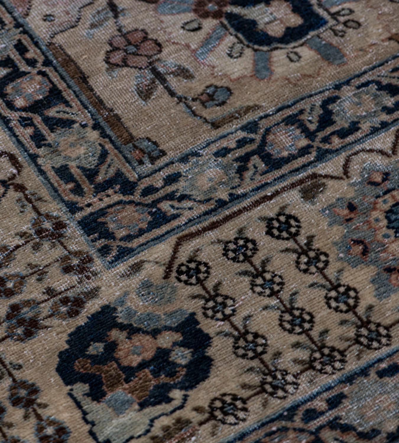 This traditional Tabriz rug has a shaded buff-brown field with an overall design of bold charcoal-black, light blue, mole-brown and ivory palmette and floral vine, in a broad pale ivory border of charcoal-black and ivory palmettes linked by angular