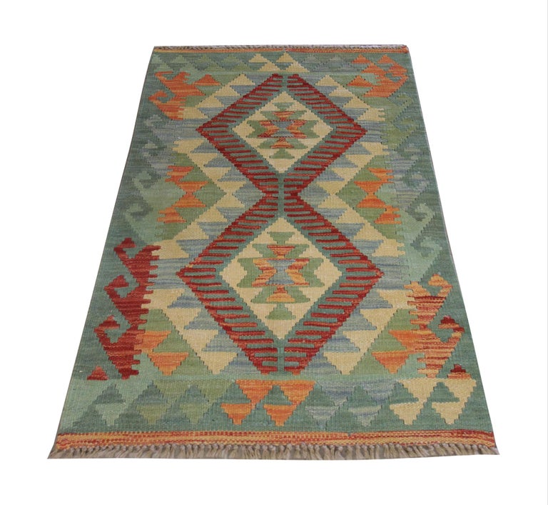 This beautiful kilim rug is a handwoven Afghan area rug constructed in the early 21st century. The design features Two large motifs that run through the centre, in accents of red and rust. A hook pattern border has then framed this. The colour
