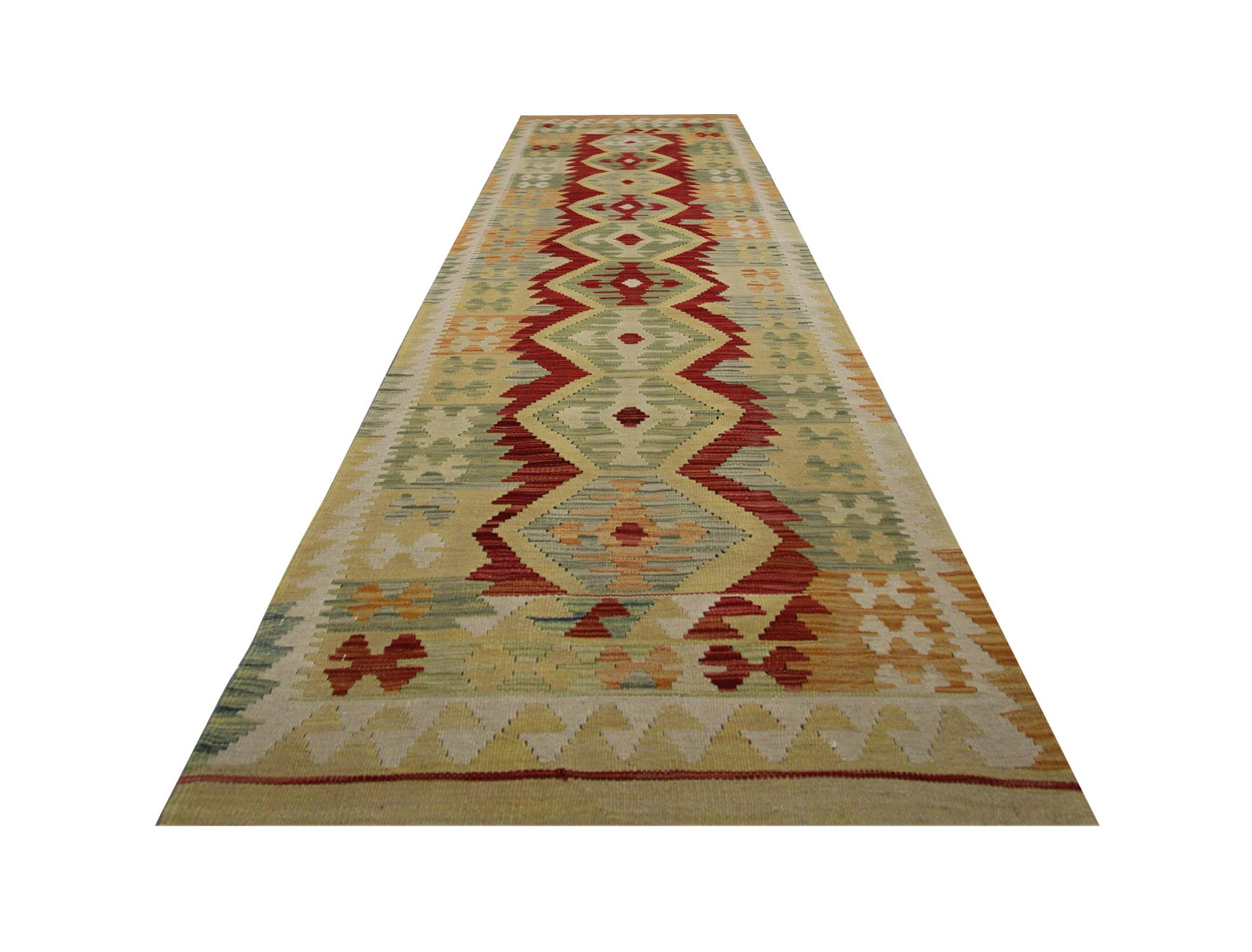 This fine wool kilim rug was woven by hand in Afghanistan in the early 21st century. The design features a bold geometric pattern woven in a repeating structure, displaying a rich colour palette including cream, red, green and beige. The colour and
