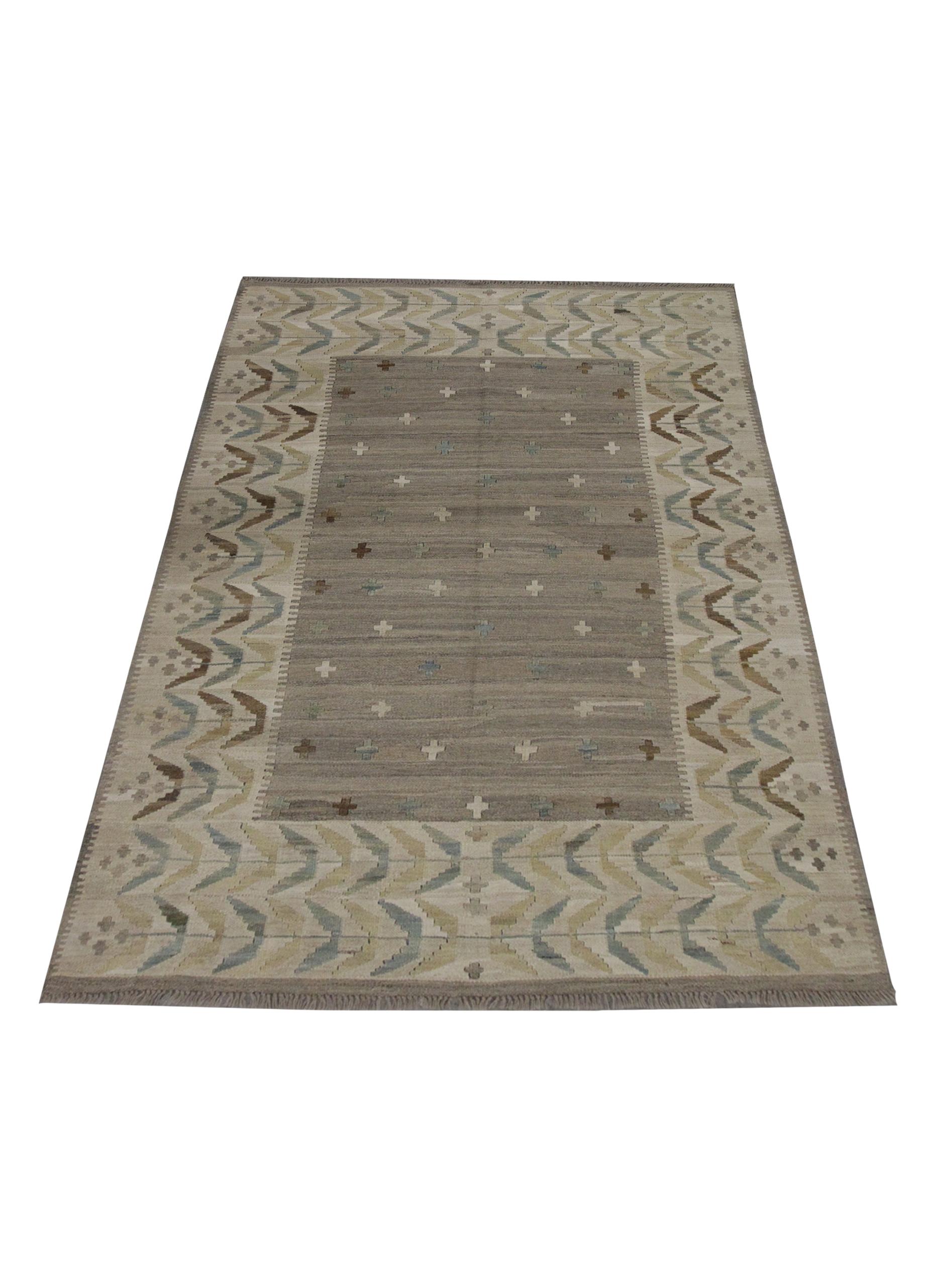 This unique wool Kilim area rug was woven in the early 21st century in Afghanistan. The design features a simple central design featuring a beige open field with Minimalist Khaki brown grey and blue cross motifs that are evenly scattered. A
