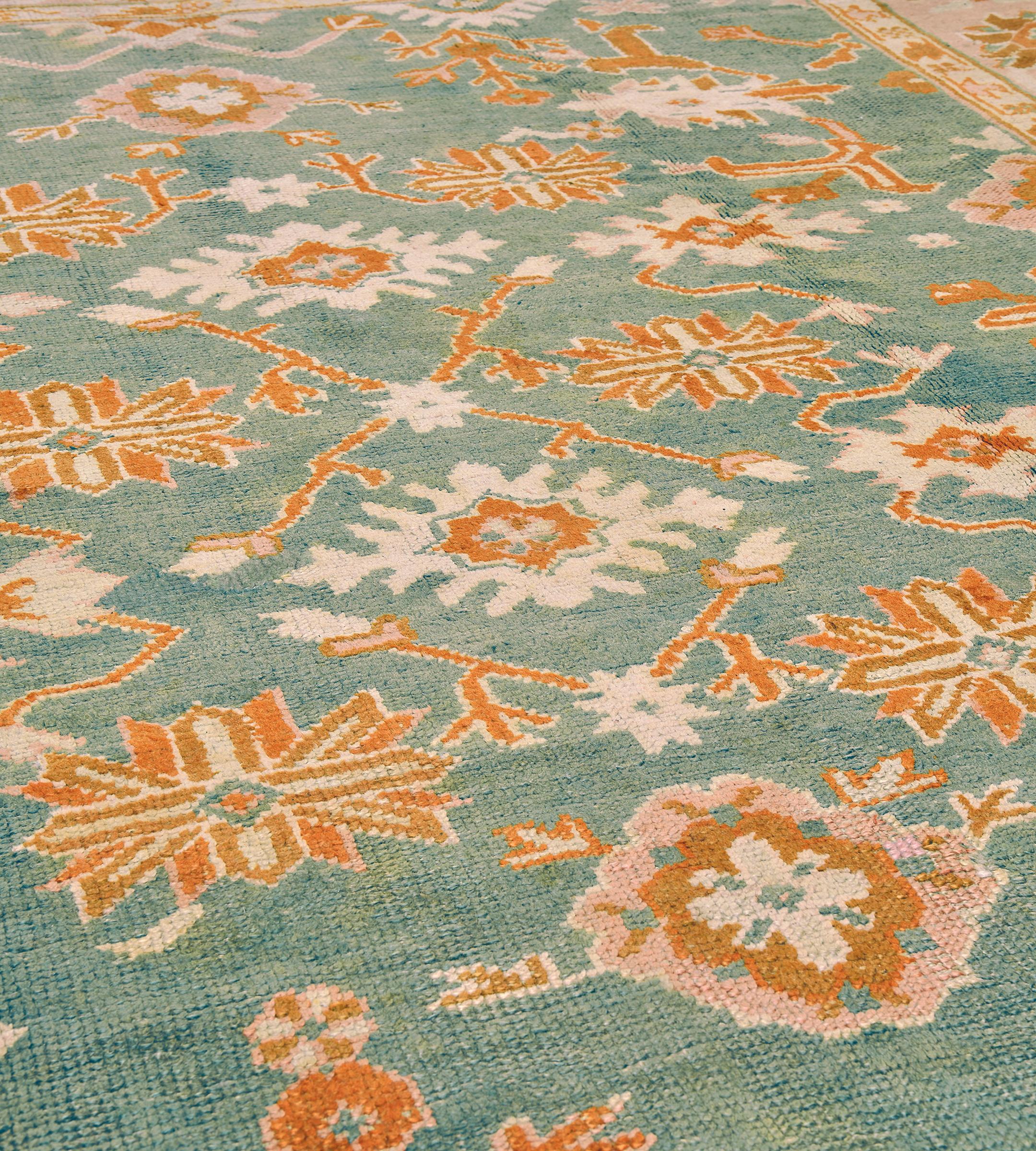 This traditional hand-woven Turkish Oushak rug has a brilliant teal field with overall design of alternating rust and ivory geometric floral motif issuing angled vines, in a shaded dusty rose stylized palmette border, between delicate vine stripes,