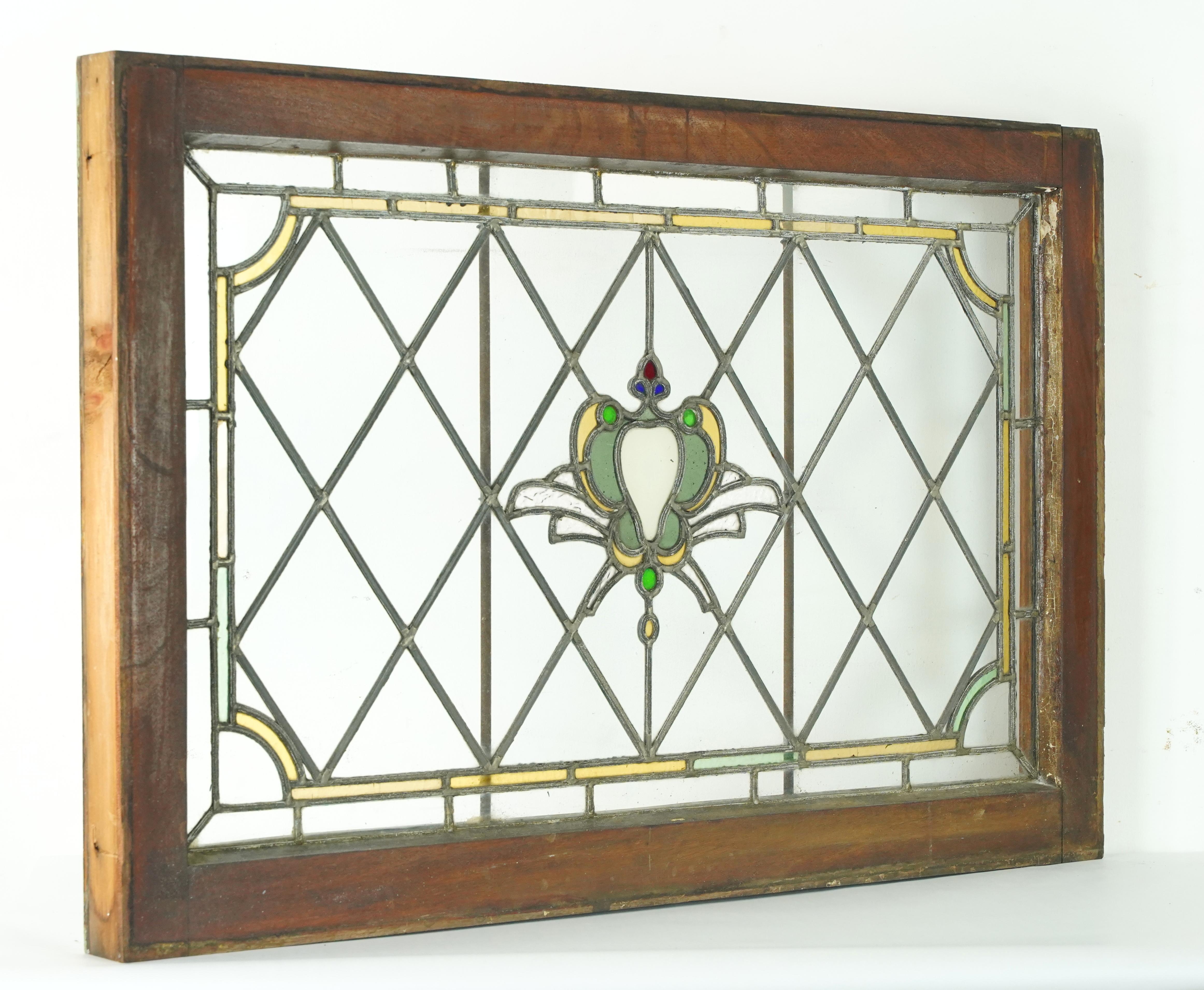 Finestra in vetro colorato piombato dei primi del Novecento di forma rettangolare con cornice in legno tinto scuro. La finestra presenta un disegno centrale a forma di cuore bianco, verde e giallo, circondato da una griglia a rombi. Il bordo del