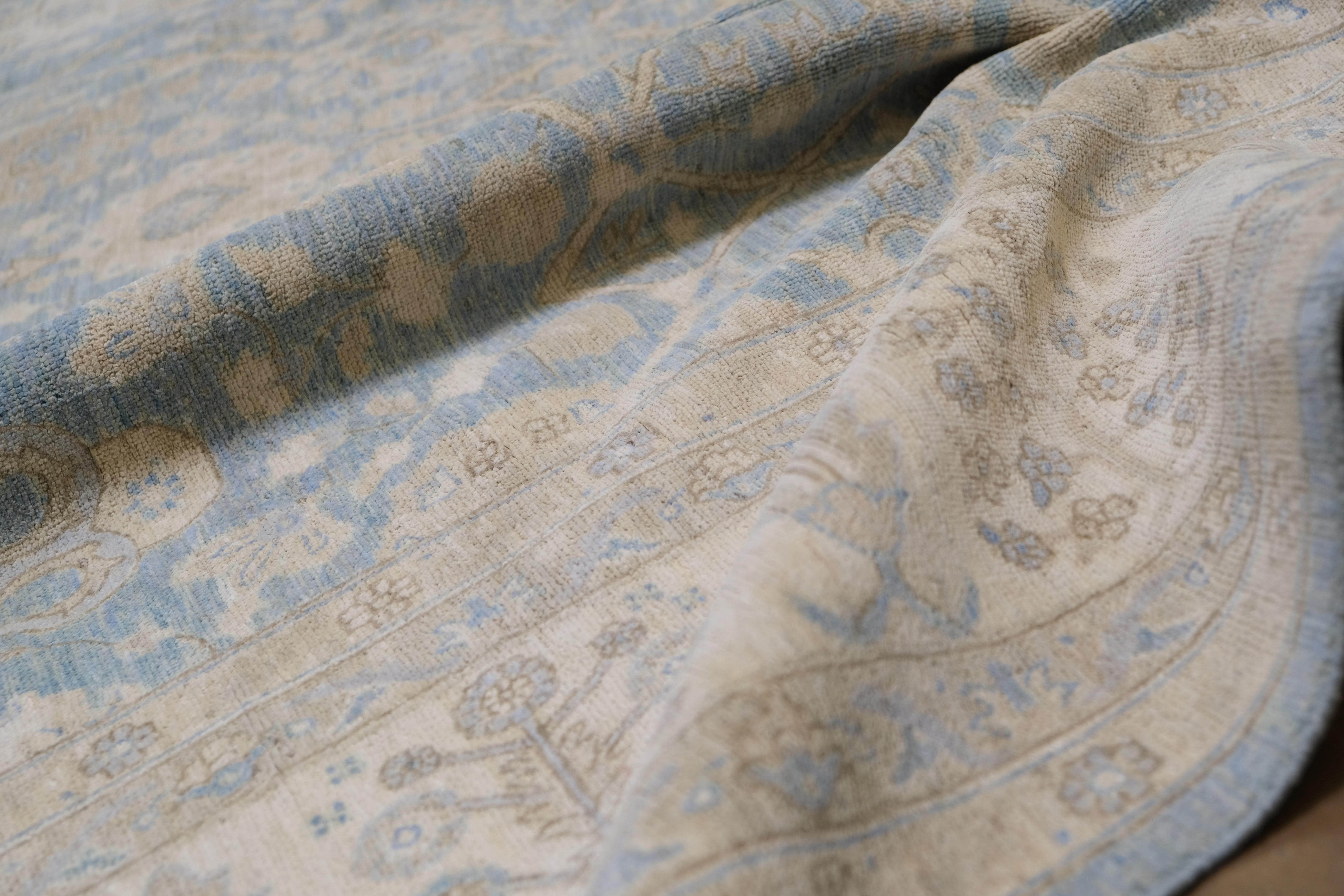 Ce superbe tapis en laine noué à la main en Afghanistan présente un motif floral complexe inspiré des motifs persans traditionnels. Son fond bleu tendre est délicatement rehaussé par des tons ivoire et beige, créant une palette harmonieuse et