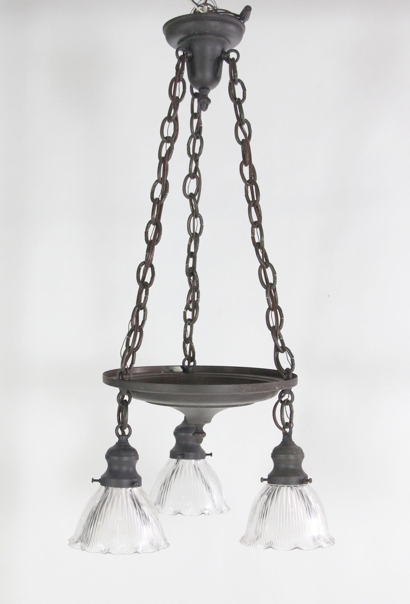 Early 1900's pendant pan light featuring 3 down lights with ruffled Holophane shades. The darkened brass fitter will come rewired which is included in price. This can be seen at our 400 Gilligan St location in Scranton, PA.

   