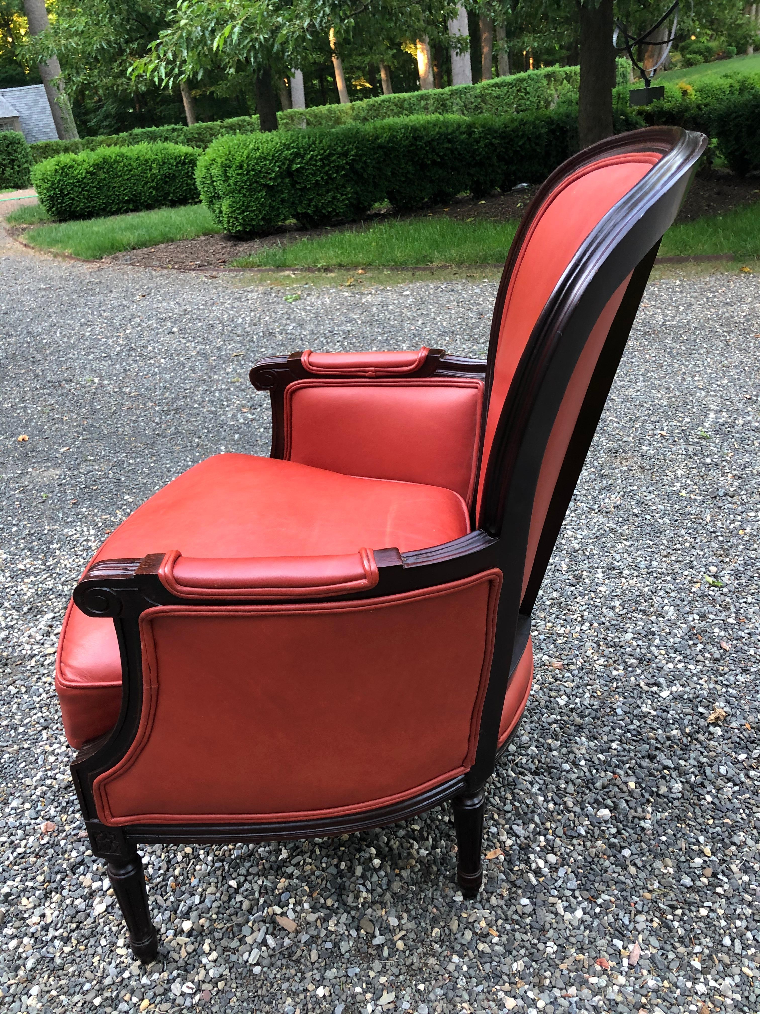 Vintage leather armchair in a fabulous shade of persimmon. The chair is constructed of mahogany and has detailed carving on arms and legs. Cushion is feather and down as indicated on tags. Extremely comfortable and adds a stylish pop of