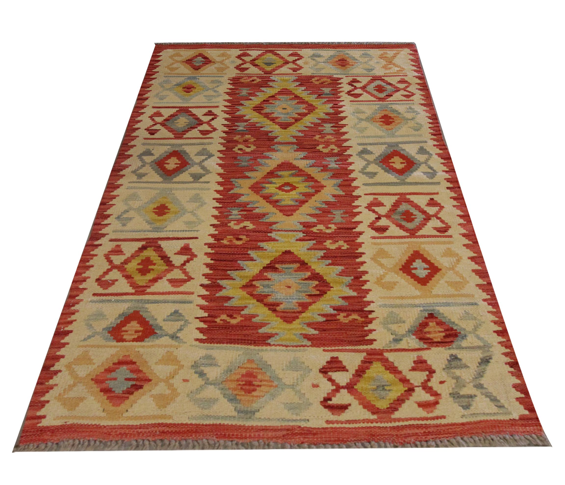 This rich red wool area rug is a handwoven kilim constructed in the early 21st century. The design features a trio of geometric motifs woven in yellow, orange, and grey accents on a rich red open field. This is then enclosed by a cream border with