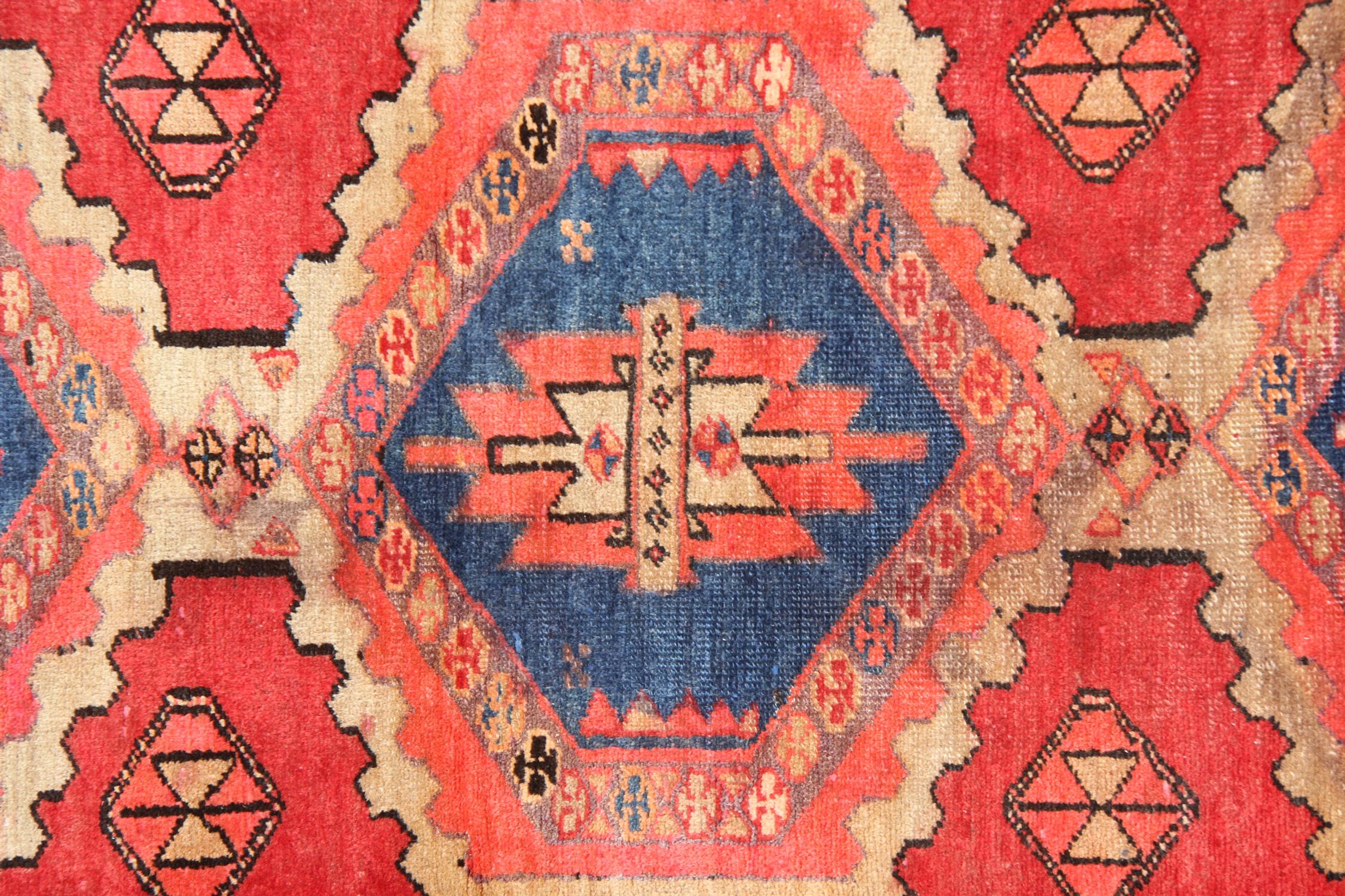 This Vintage Rug was constructed by hand with fine organic materials. Woven with a traditional design and colour palette. Featuring a rich red background and highly decorative repeat hexagon medallion design with blue and cream accents through the