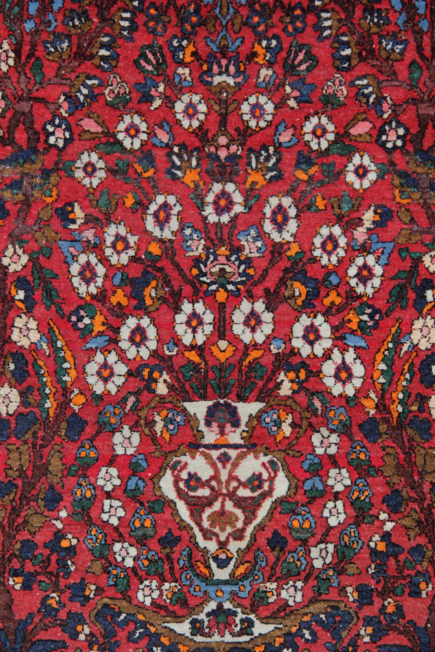 This fine antique rug was woven in the late 19th century, circa 1890 and features a beautiful red field with a highly decorative central design. With a vase surrounded by floral and foliate motifs and scrolls that run through the centre and a highly