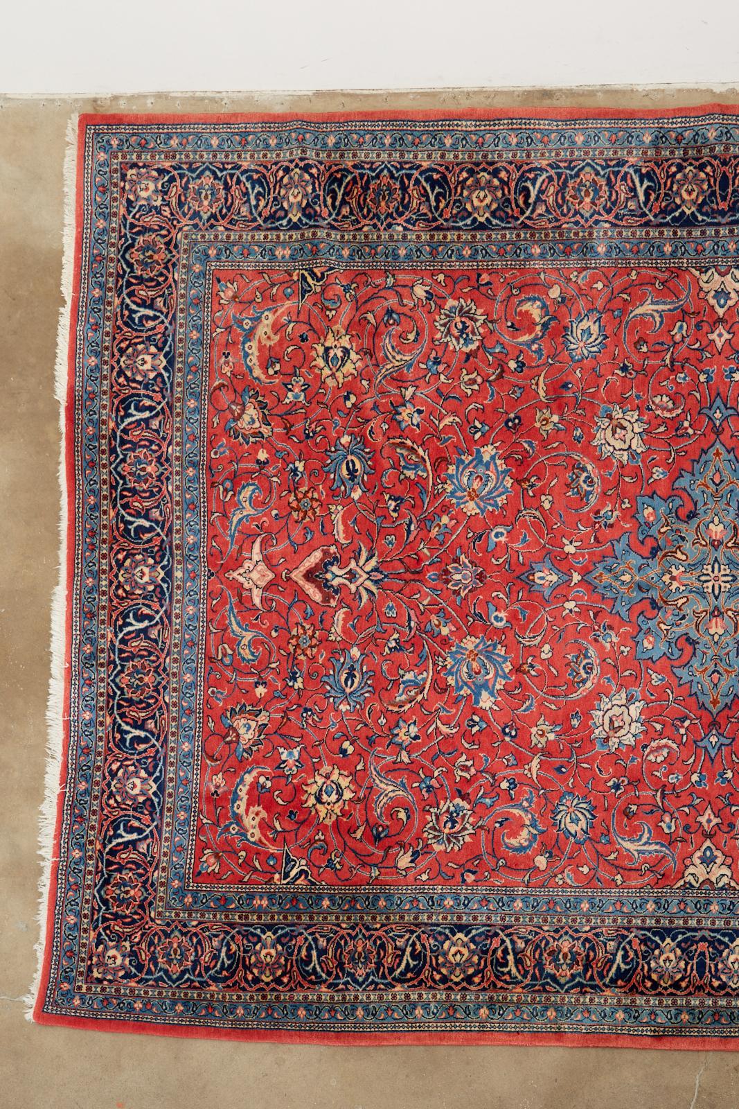 Luxurious traditional Persian Sarouk rug featuring a star shaped medallion over a vibrant ruby red field. The rug has a velvety soft hand knotted wool pile with designs of scrolling floral vines and stems. The borders have a deep powder blue and