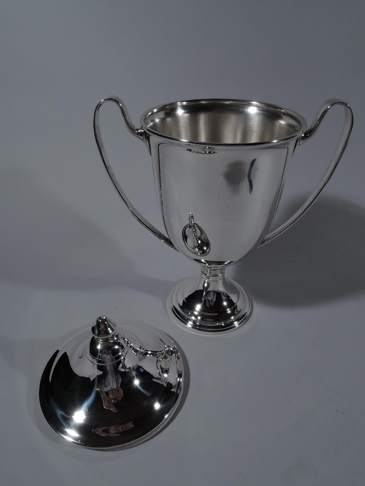 Classical sterling silver trophy cup. Traditional amphora urn with high-looping side handles and stepped and raised foot. Cover domed with engraved bands and acorn finial. A nice cup with lots of room for engraving. Marked “Sterling / By / Fina”.