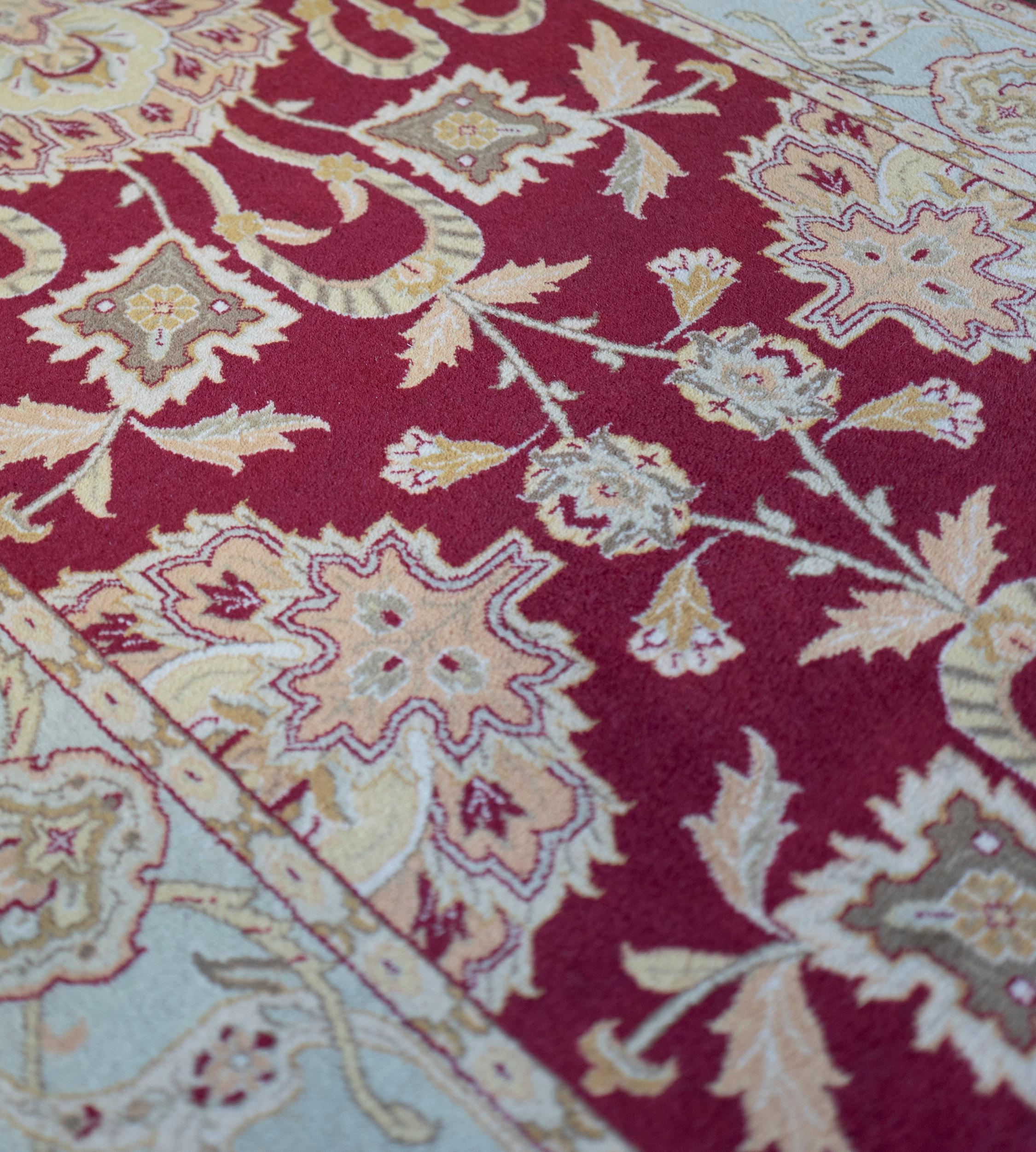 This revival Agra runner features a burgundy-red field with a central column of shaded pink, green and ivory palmettes linked by scrolling floral vine and similar part-palmettes, in a light blue border of buff-brown lozenges linked by scrolling
