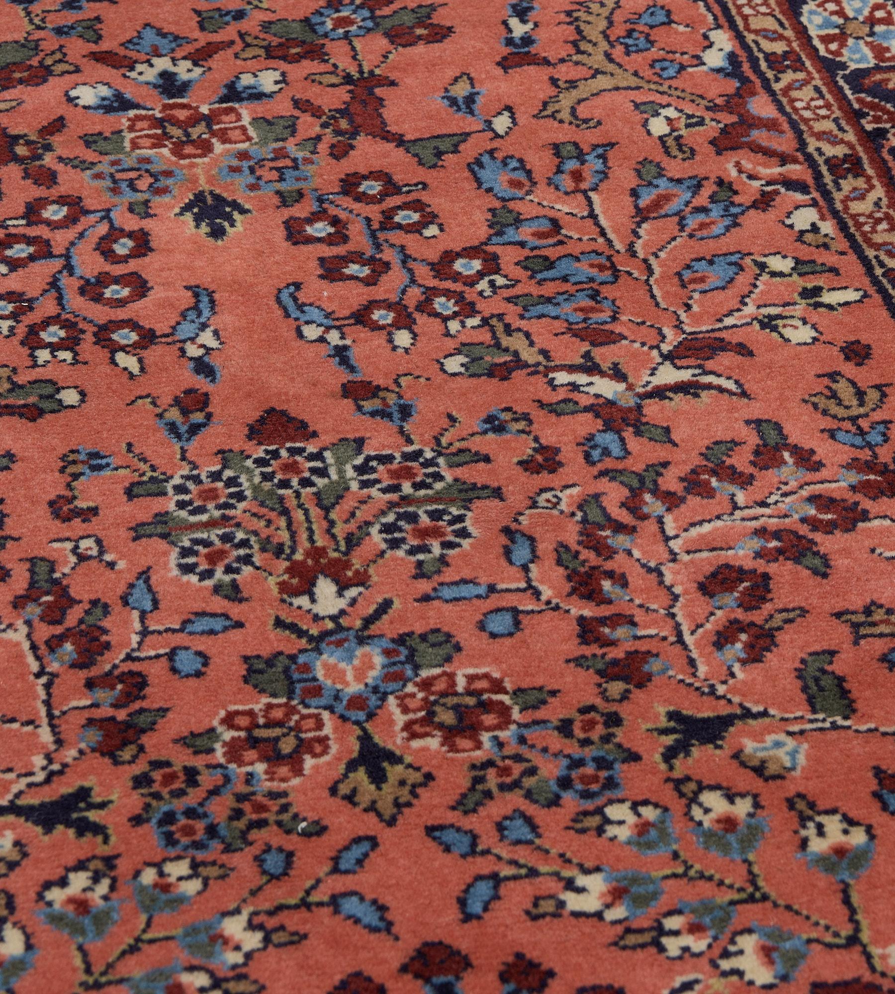 Ce chemin de table persan vintage présente un champ rouge terracotta doux avec, à chaque extrémité, un vase orné d'une délicate gerbe florale entourée d'autres gerbes florales en volutes et de plantes en fleurs, dans une bordure bleu indigo profond