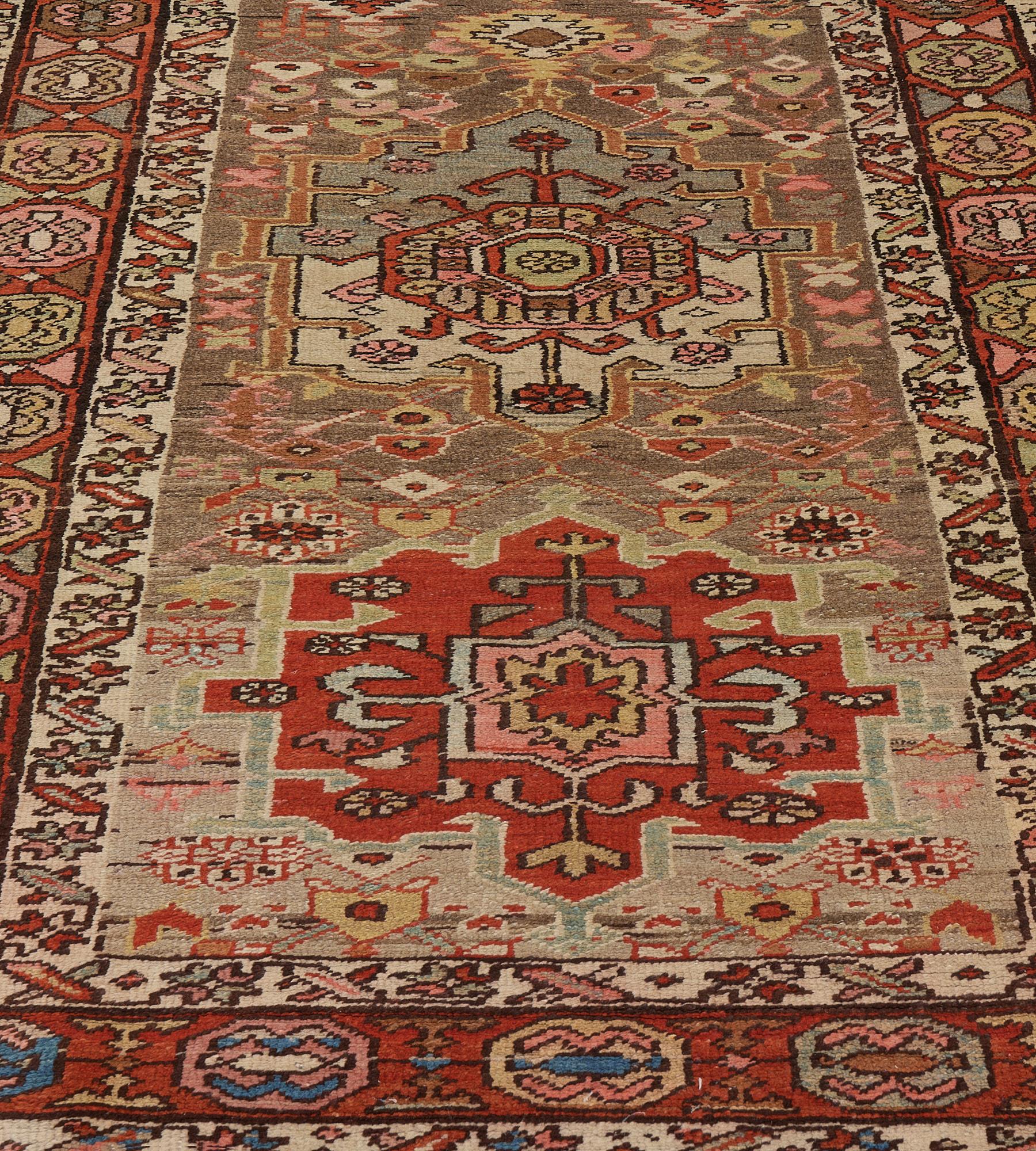 This antique Serab runner features a shaded mole-grey field scattered with polychrome floral motifs and lozenges around a central column of six polychrome shield lozenges each with a central panel containing a floral motif surrounded by various