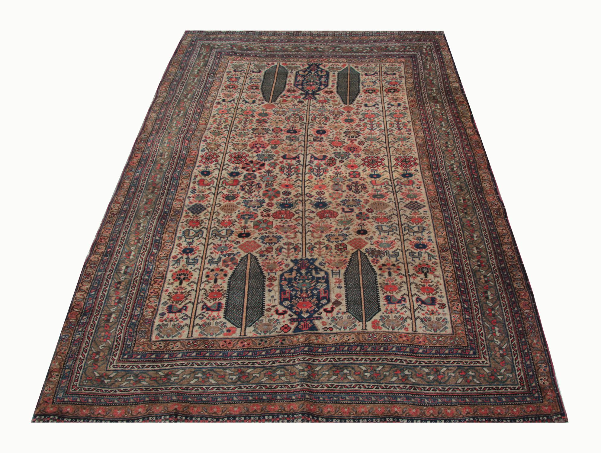 This beautiful antique wool area rug features a bold floral design woven symmetrically with tribal motifs throughout. Featuring a cream background with brown, pink, blue, and beige accents that make up the design. Both the colour palette and