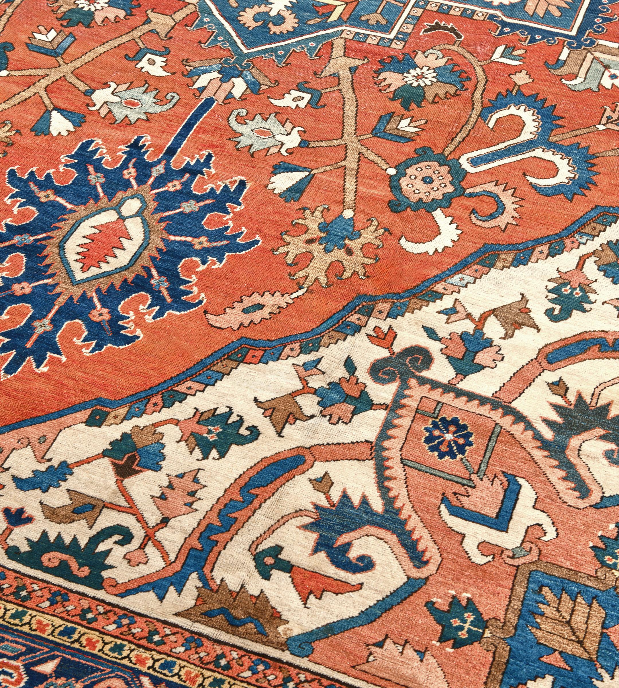 This traditional hand-woven Persian Serapi rug has a brick field of meandering floral motif enclosing a bold indigo arabesque medallion with similar motif, radiating from a central rosette roundel, in an indigo turtle-palmette border, between