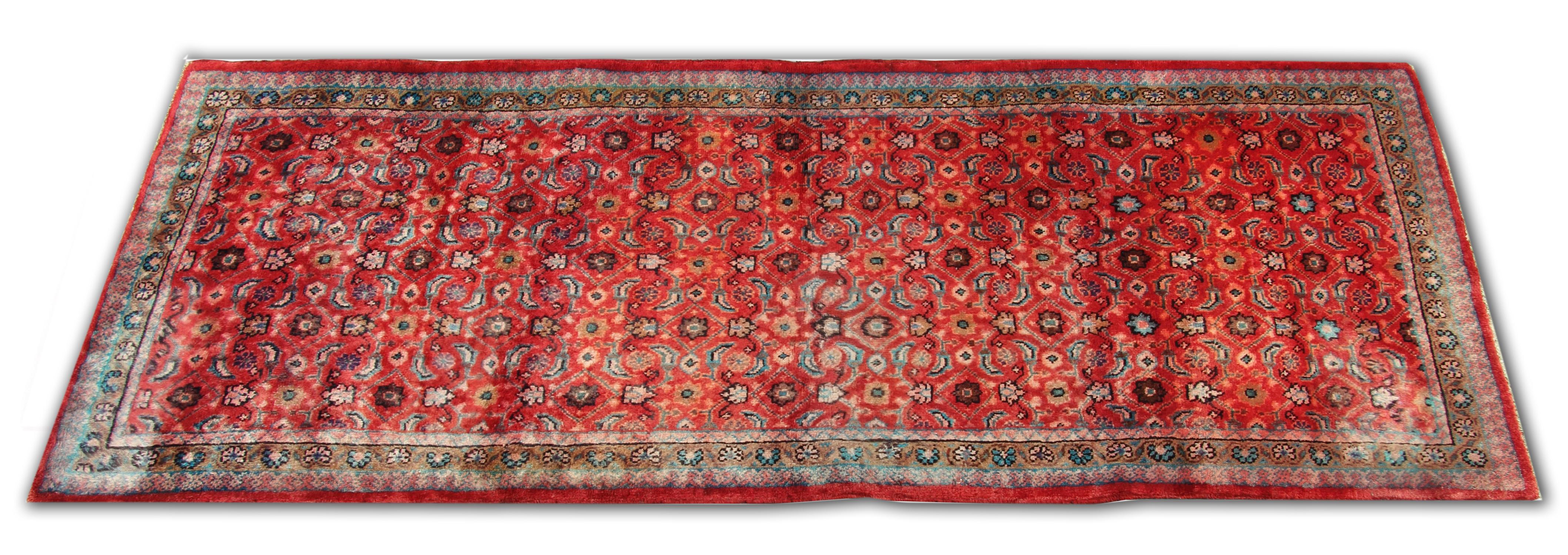 This fine red wool runner rug is a traditional vintage carpet woven by hand in the late 20th century. The design features a repeating pattern and a layered border that encloses the design. Woven in accents of blue, brown and ivory on a rich red