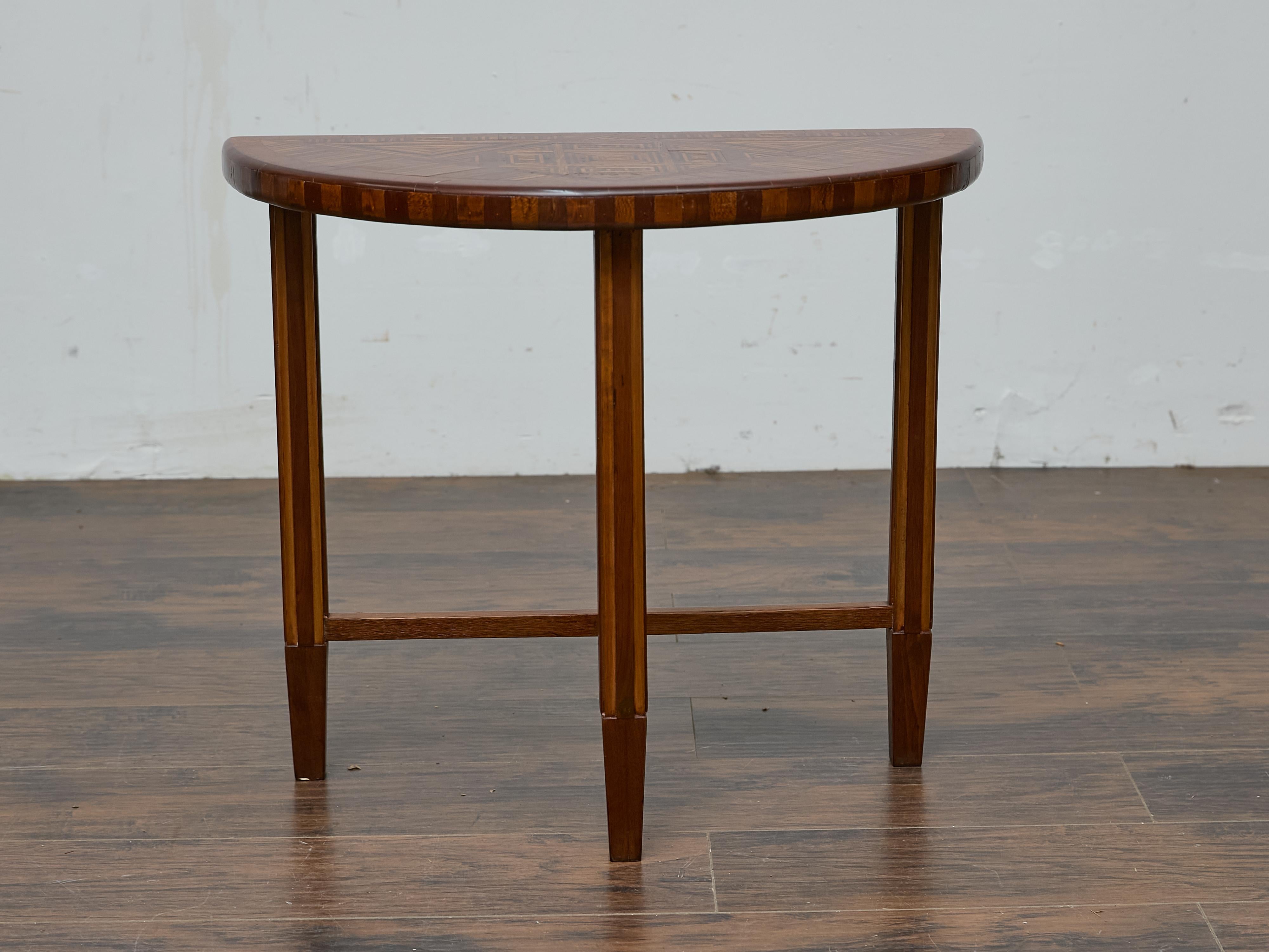 Cette table demi-lune du début du XXe siècle est un exemple frappant de l'artisanat du Tramp Art. Elle se distingue par ses incrustations géométriques complexes et sa présence sculpturale. Le plateau de la table présente une marqueterie élaborée, un